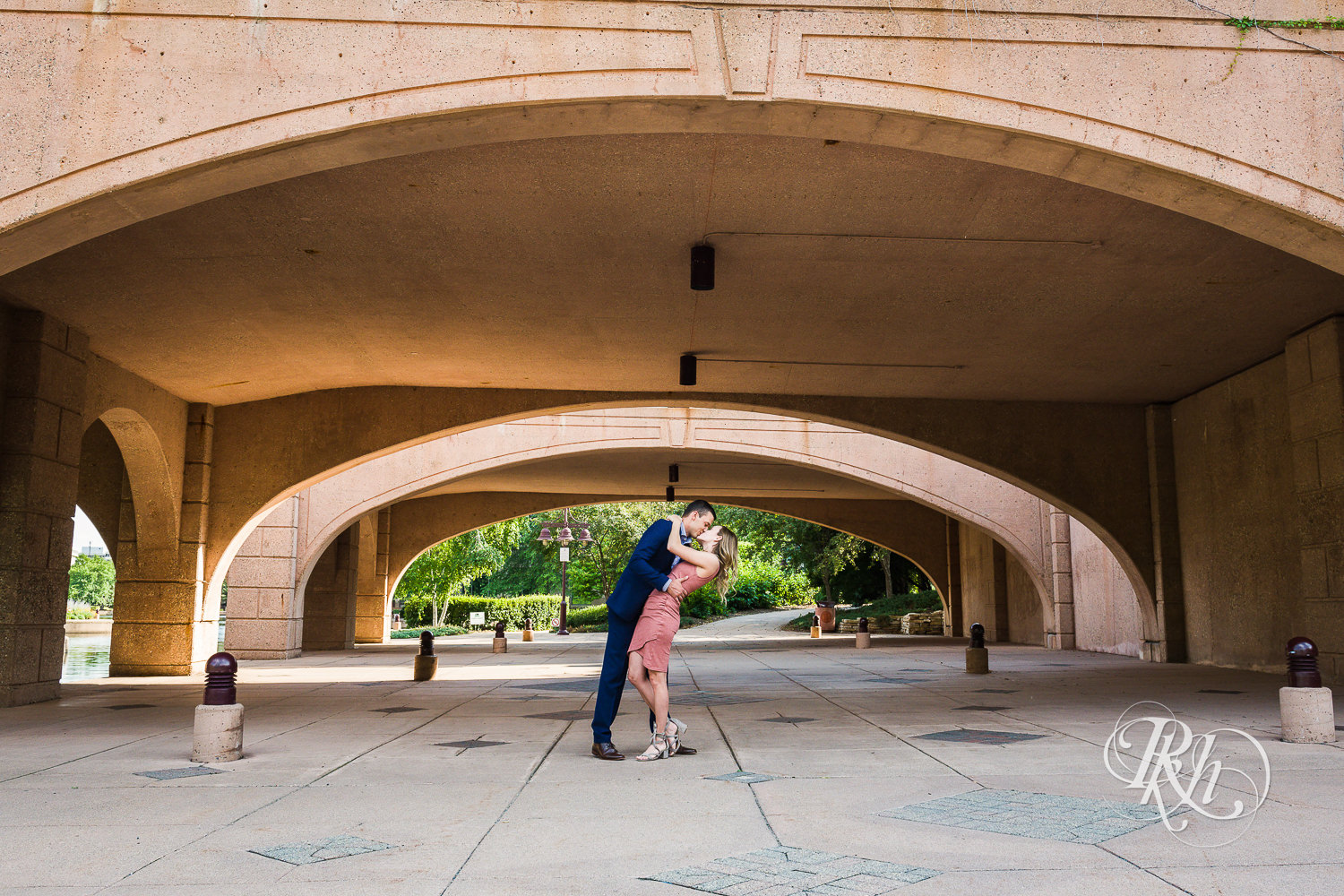 Man in blue suit and woman in pink dress kiss during Centennial Lakes Park engagement photography in Edina, Minnesota.