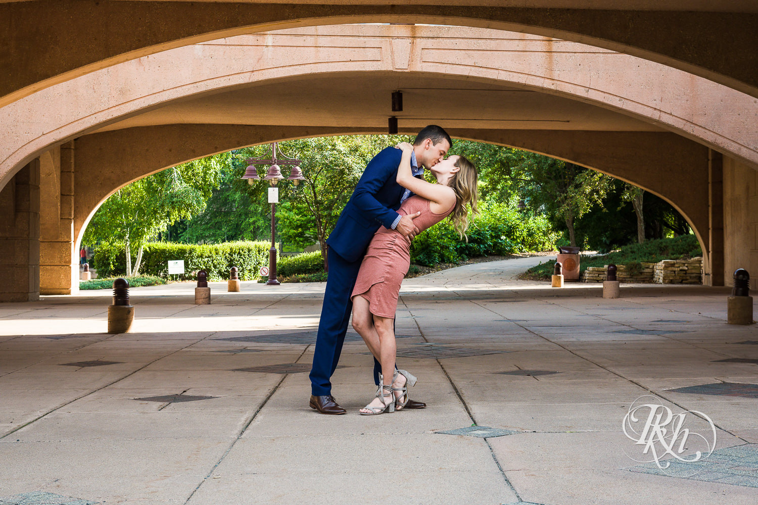 Man in blue suit and woman in pink dress kiss during Centennial Lakes Park engagement photography in Edina, Minnesota.