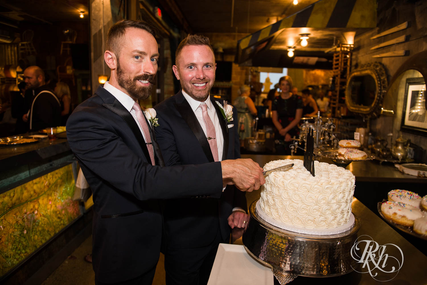 Grooms cut cake during wedding reception speeches at Warehouse Winery wedding in Saint Louis Park, Minnesota.
