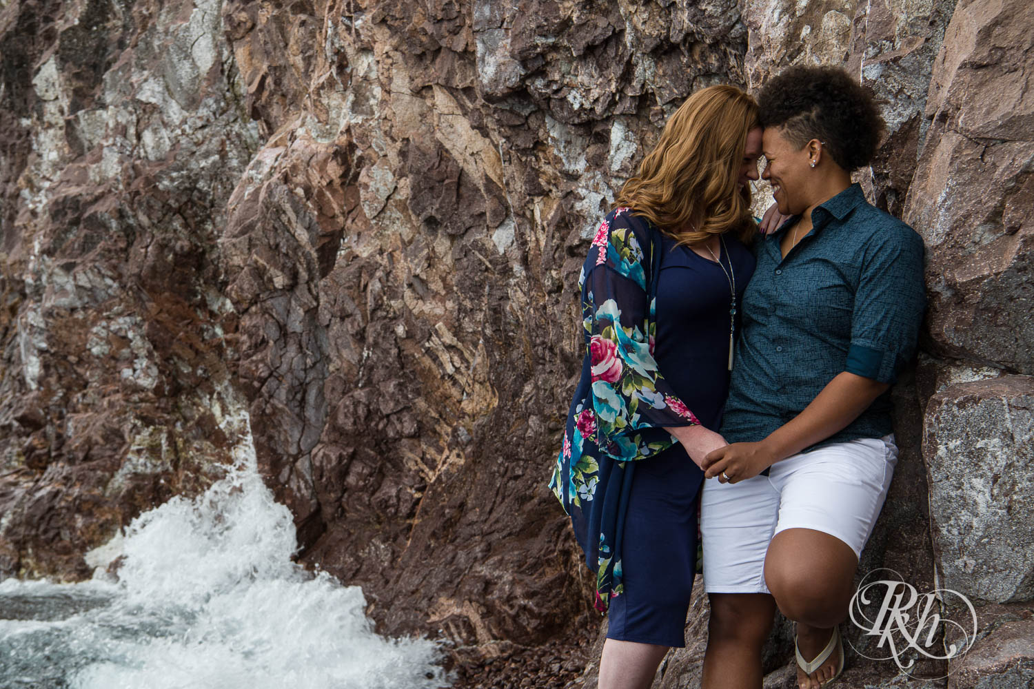 Two women smile during lesbian black beach engagement photography