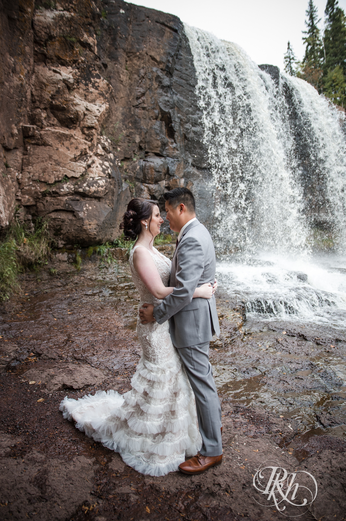 Bride and groom smile in front of waterfall at Gooseberry Falls in Two Harbors, Minnesota.