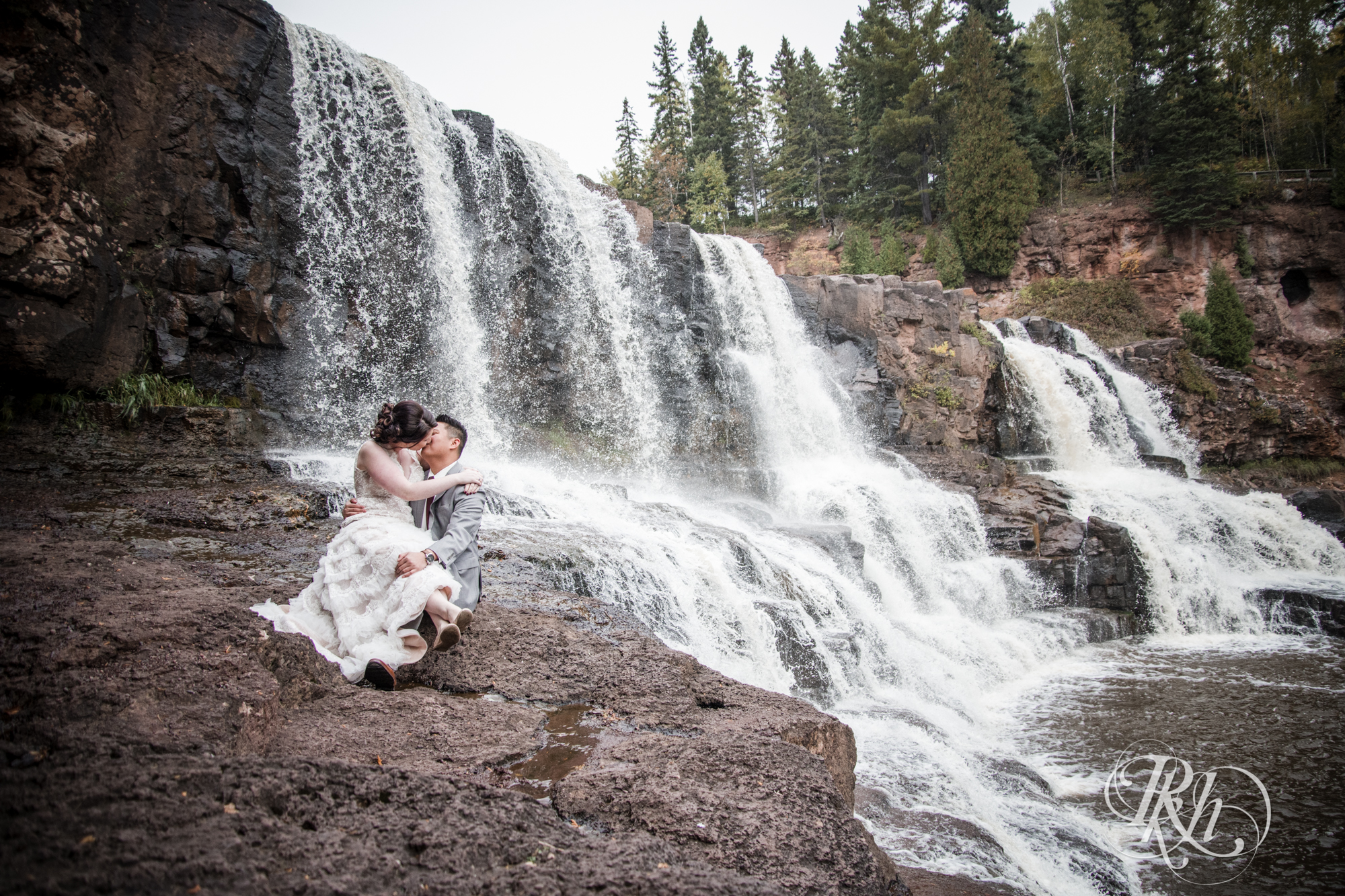 Bride and groom kiss in front of waterfall at Gooseberry Falls in Two Harbors, Minnesota.