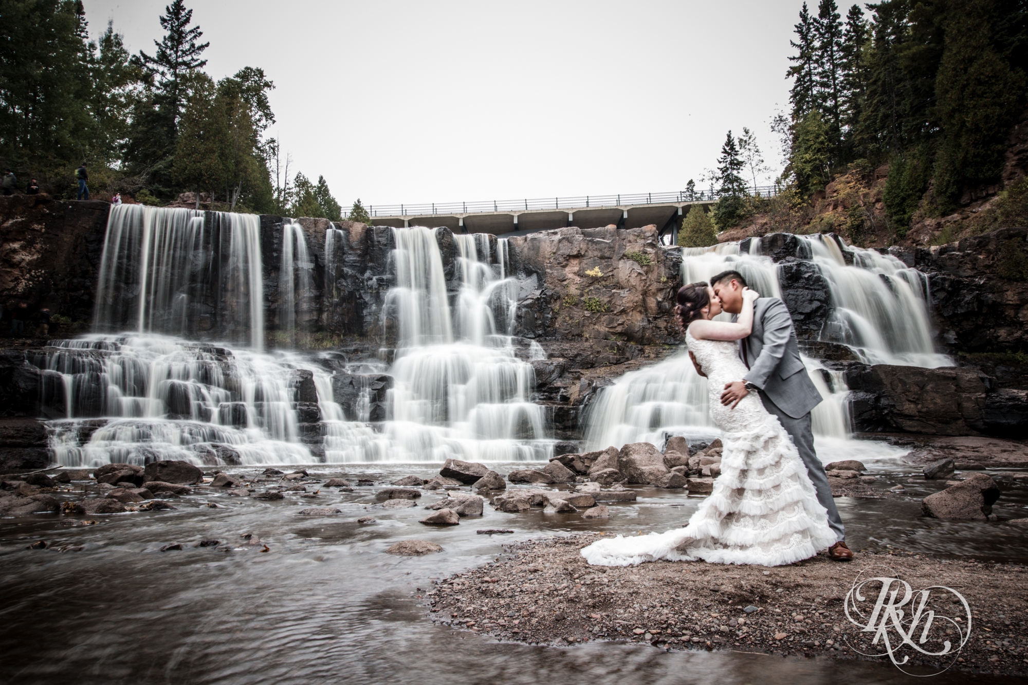 Bride and groom kiss in front of waterfall at Gooseberry Falls in Two Harbors, Minnesota.
