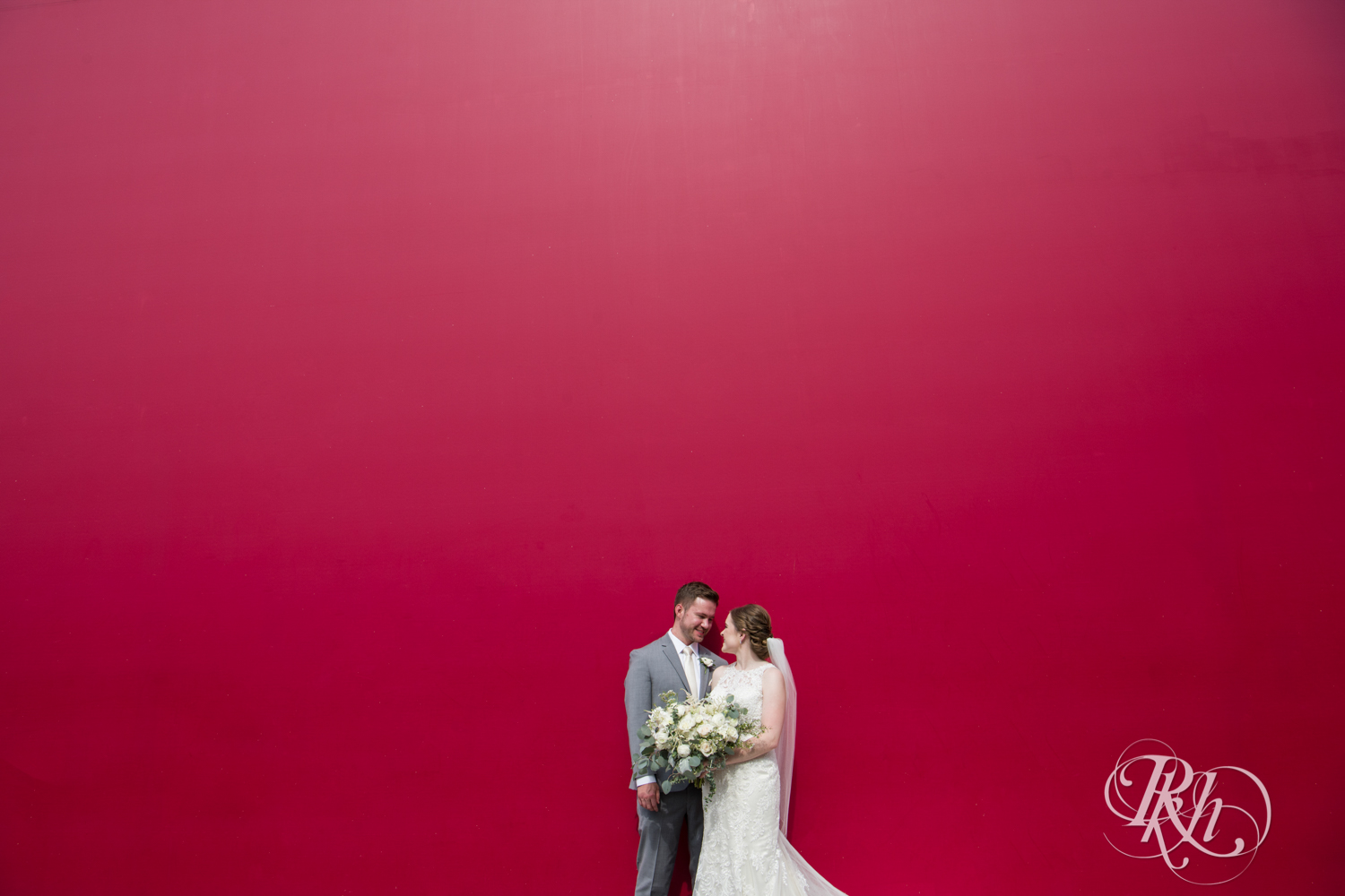 bride and groom standing in front of red wall