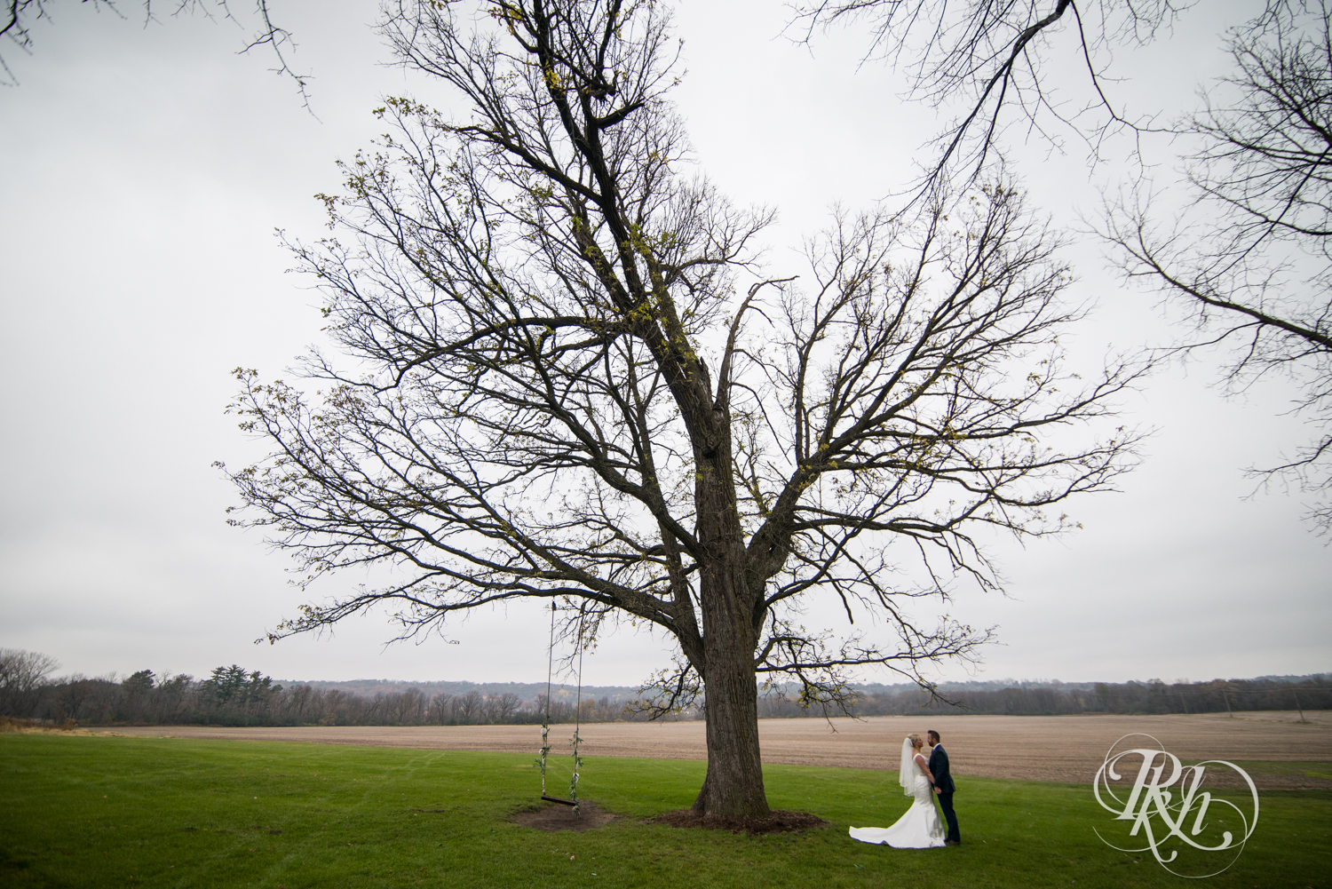 Bride and groom stand under tree at Mayowood Stone Barn in Rochester, Minnesota.