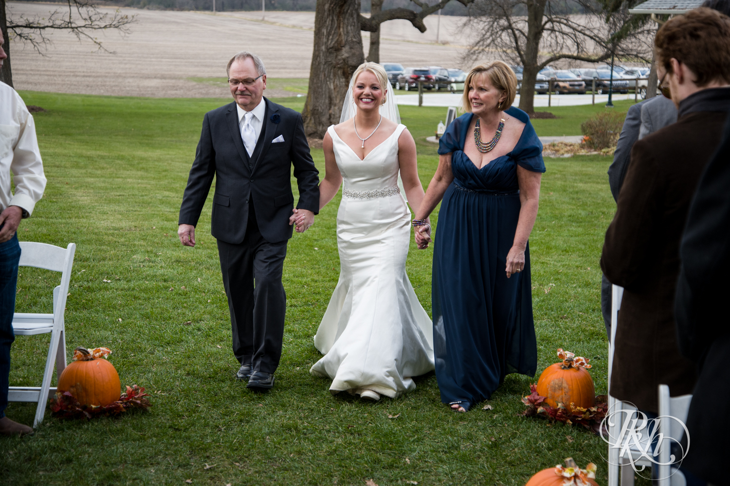 Bride walks down the aisle with mom and dad at Mayowood Stone Barn in Rochester, Minnesota.