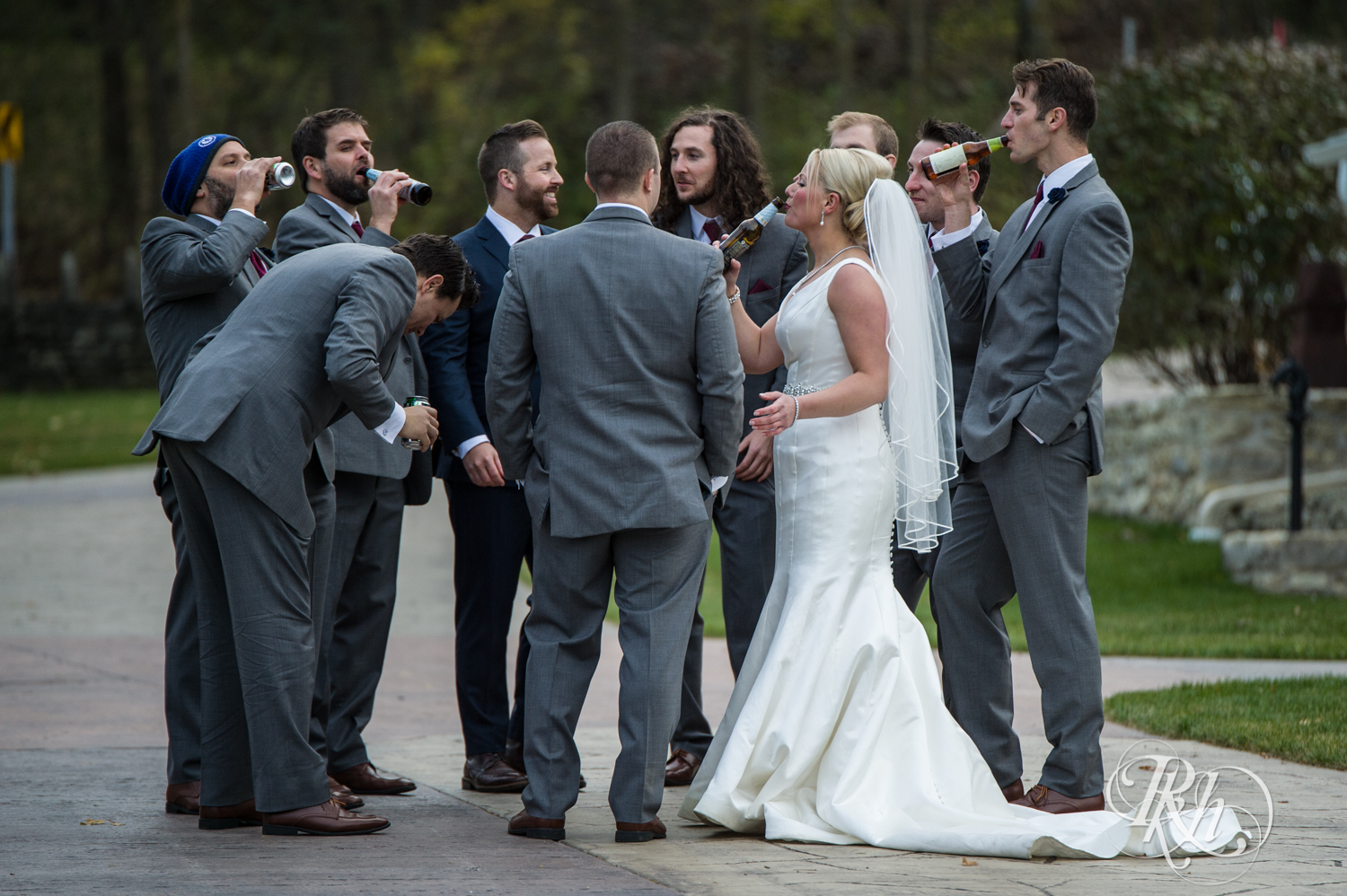 Bride drinks beer with all the groomsmen at wedding reception at Mayowood Stone Barn in Rochester, Minnesota.