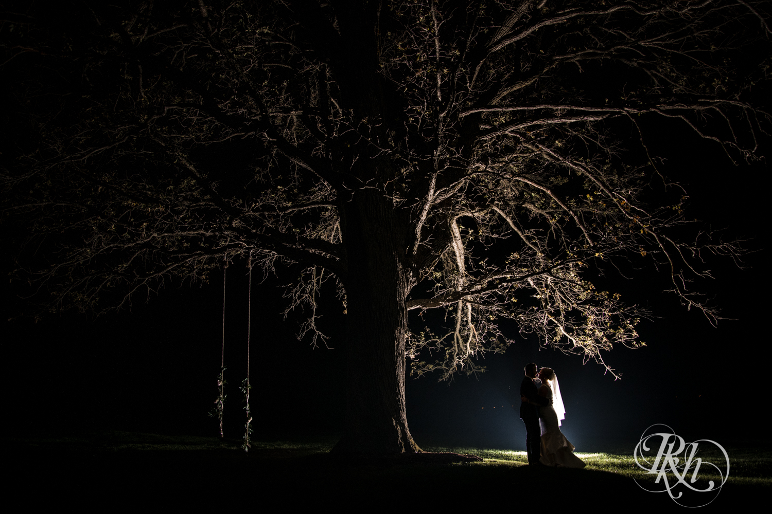 Bride and groom kiss at night under tree at Mayowood Stone Barn in Rochester, Minnesota.