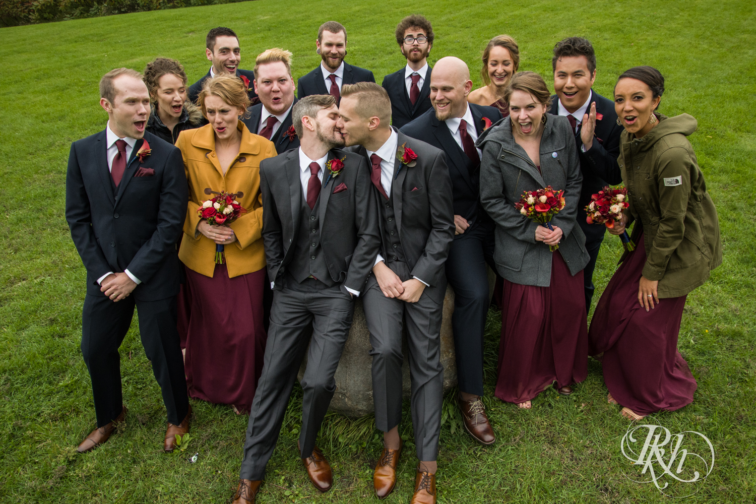 Wedding party smiles while grooms kiss at Bohemian Flats Park in Minneapolis, Minnesota for Minnesota LGBT wedding photographer.