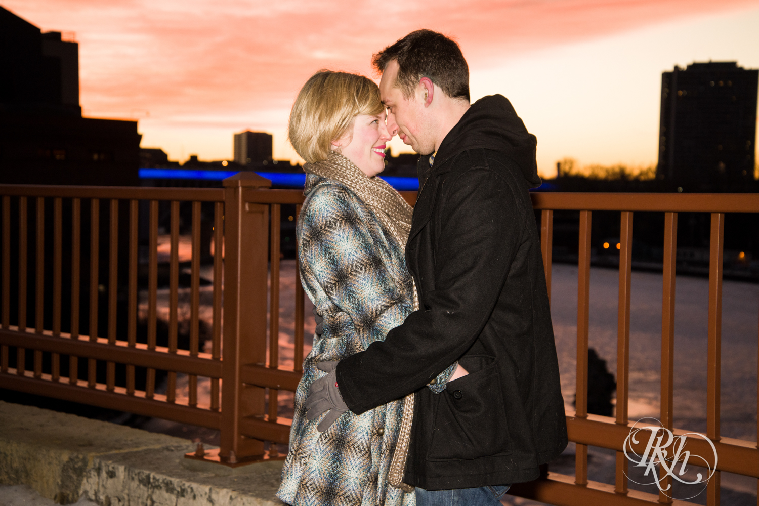 Man and woman smile during sunrise engagement photography on Stone Arch Bridge in Minneapolis, Minnesota.