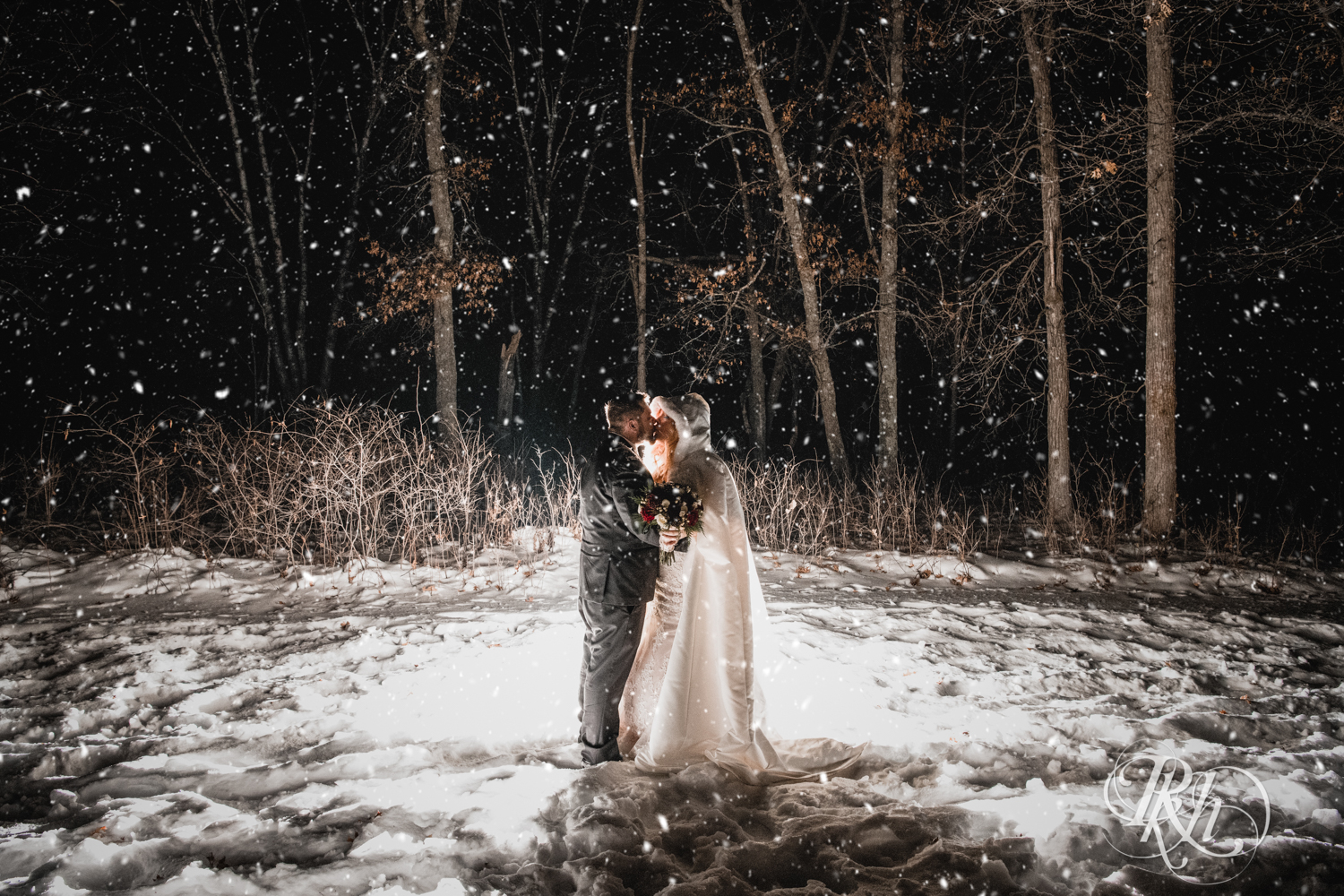 Bride and groom kiss in falling snow during winter wedding at Whitefish Lodge in Crosslake, Minnesota.