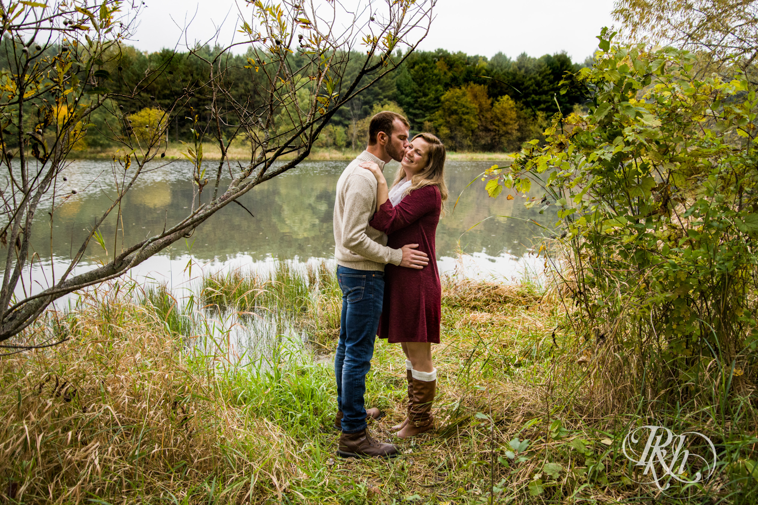 Man in sweater and woman in red dress kiss at Lebanon Hills Regional Park in Eagan, Minnesota.