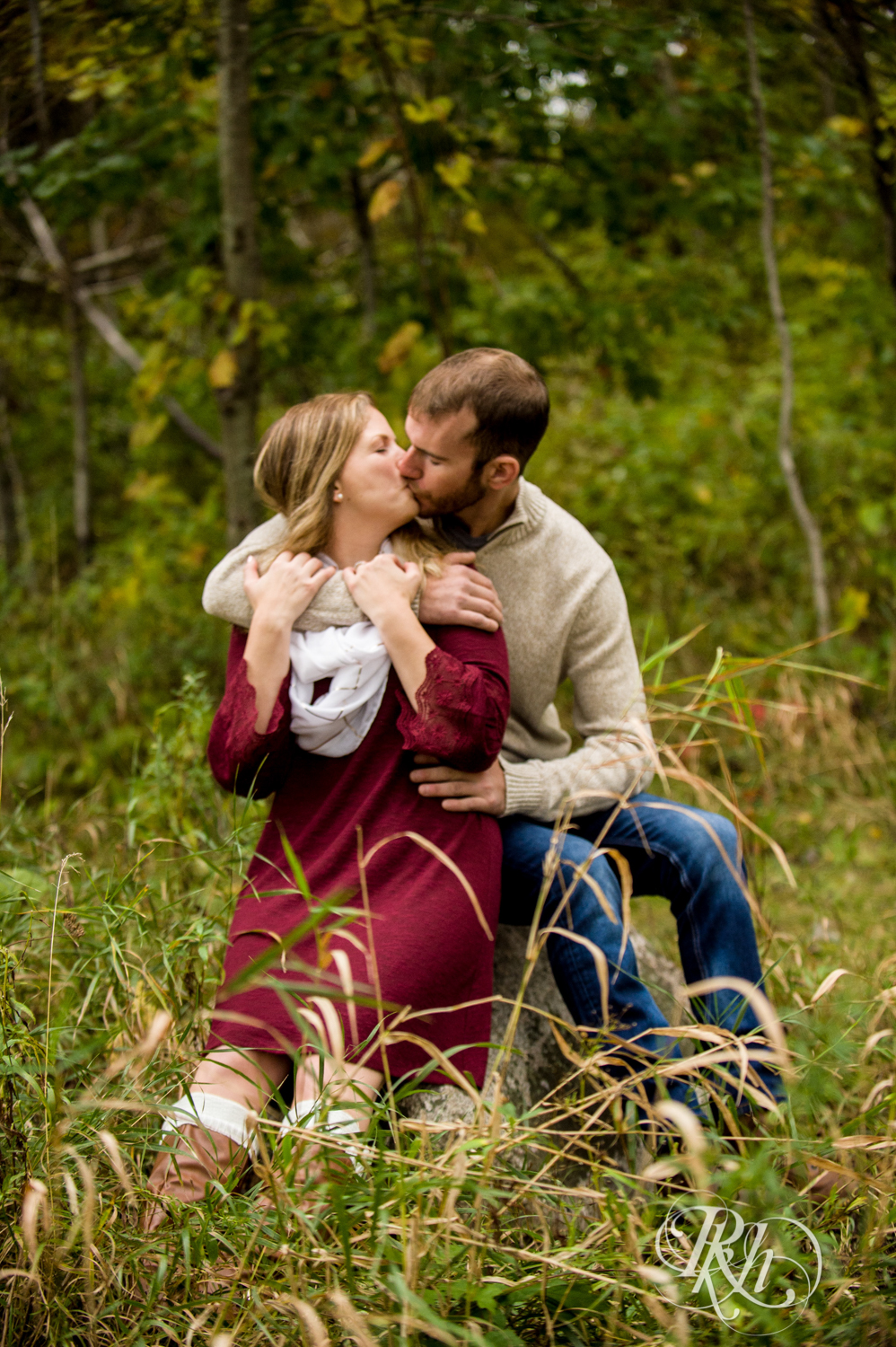 Man in sweater and woman in red dress kiss at Lebanon Hills Regional Park in Eagan, Minnesota.