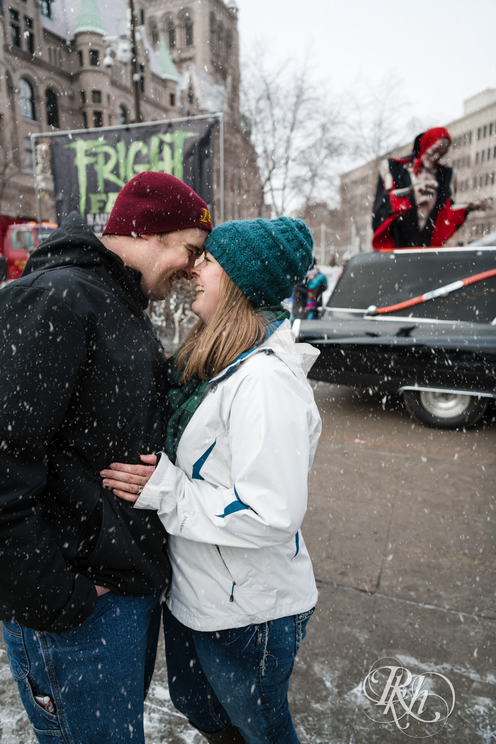 Man and woman laugh in the falling snow during engagement photography in Saint Paul, Minnesota.