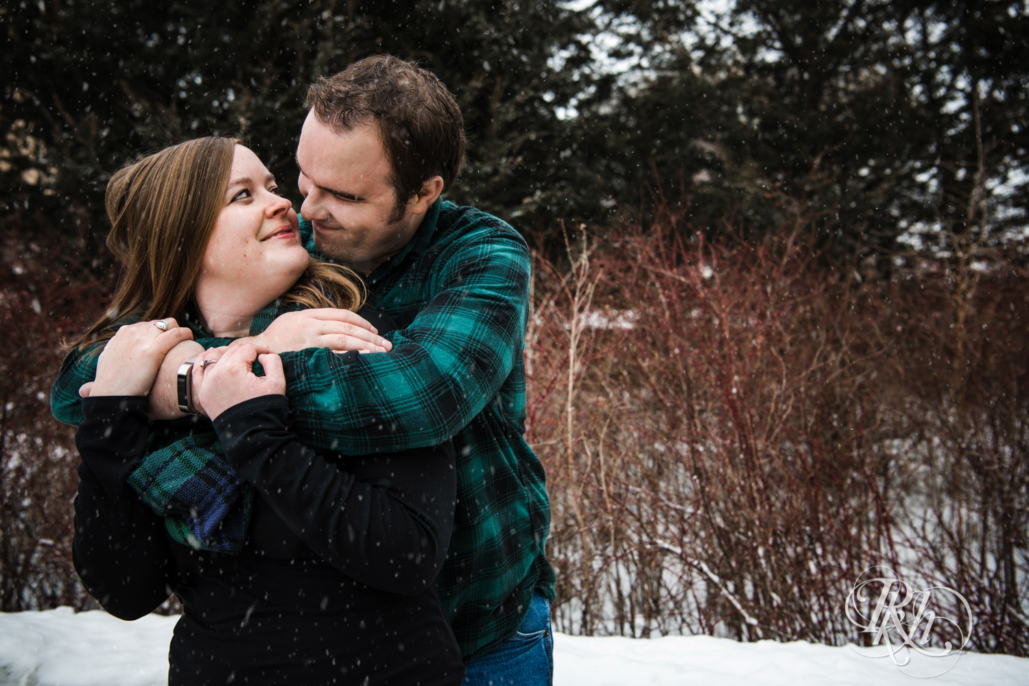 Man and woman snuggle in the falling snow during engagement photography in Saint Paul, Minnesota.