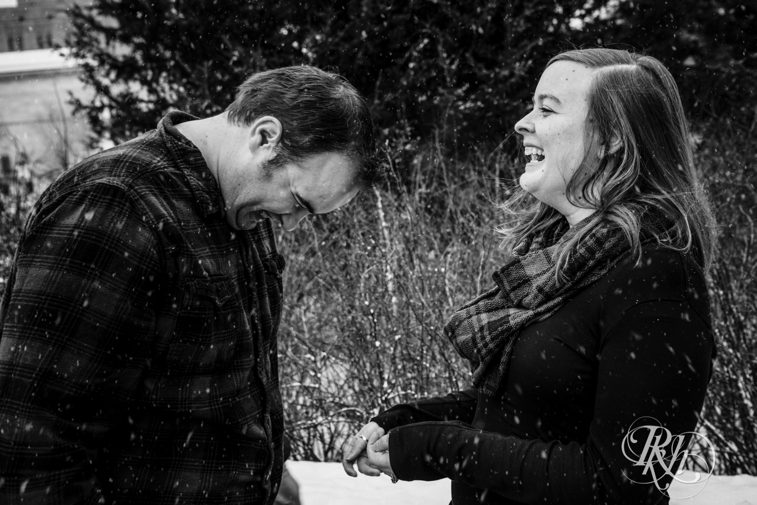 Man and woman laugh in the falling snow during engagement photography in Saint Paul, Minnesota.