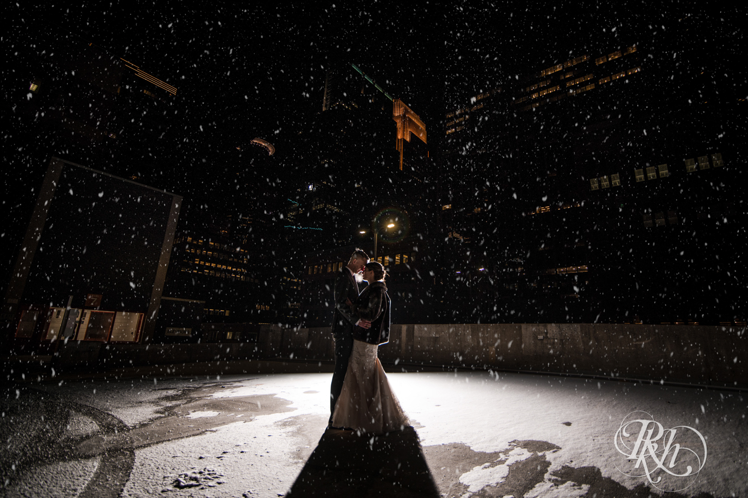 Bride and groom kiss in the falling snow on the roof of the Lumber Exchange Event Center in Minneapolis, Minnesota.