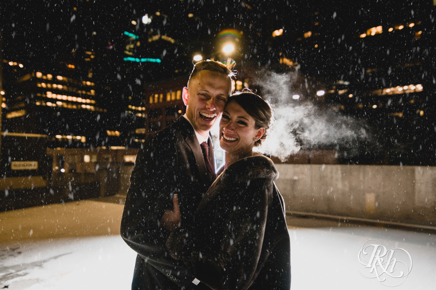 Bride and groom laugh in the falling snow on the roof of the Lumber Exchange Event Center in Minneapolis, Minnesota.