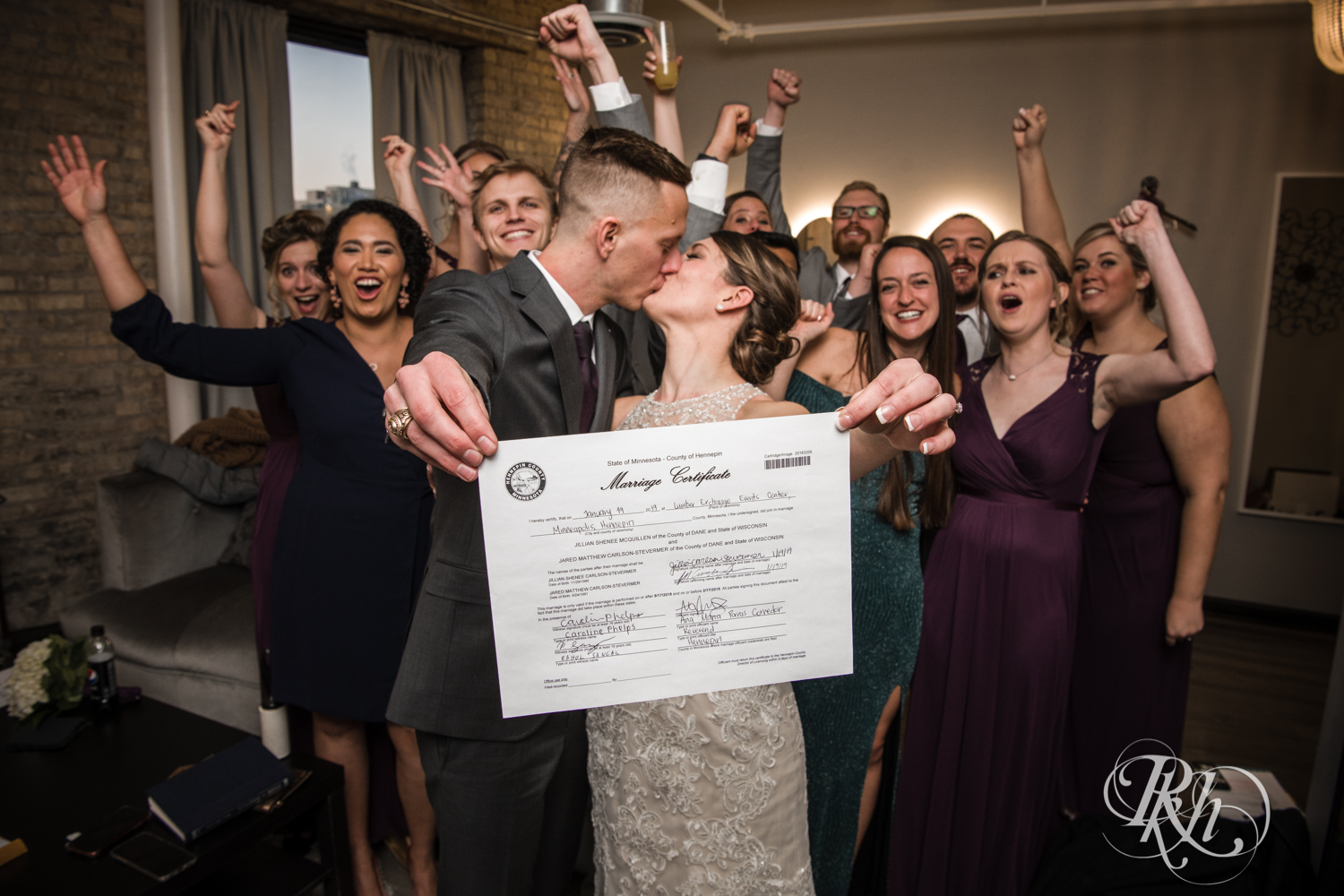 Bride and groom kiss behind marriage certificate at the Lumber Exchange Event Center in Minneapolis, Minnesota.