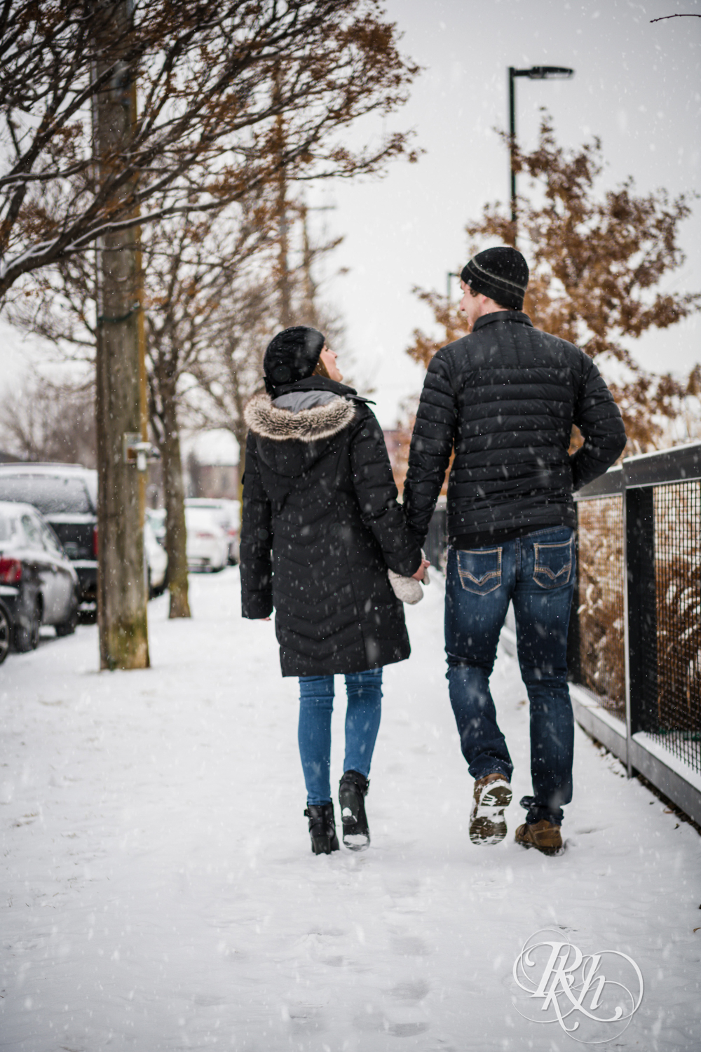 Man and woman walk in the falling snow during winter engagement photos in Saint Paul, Minnesota.