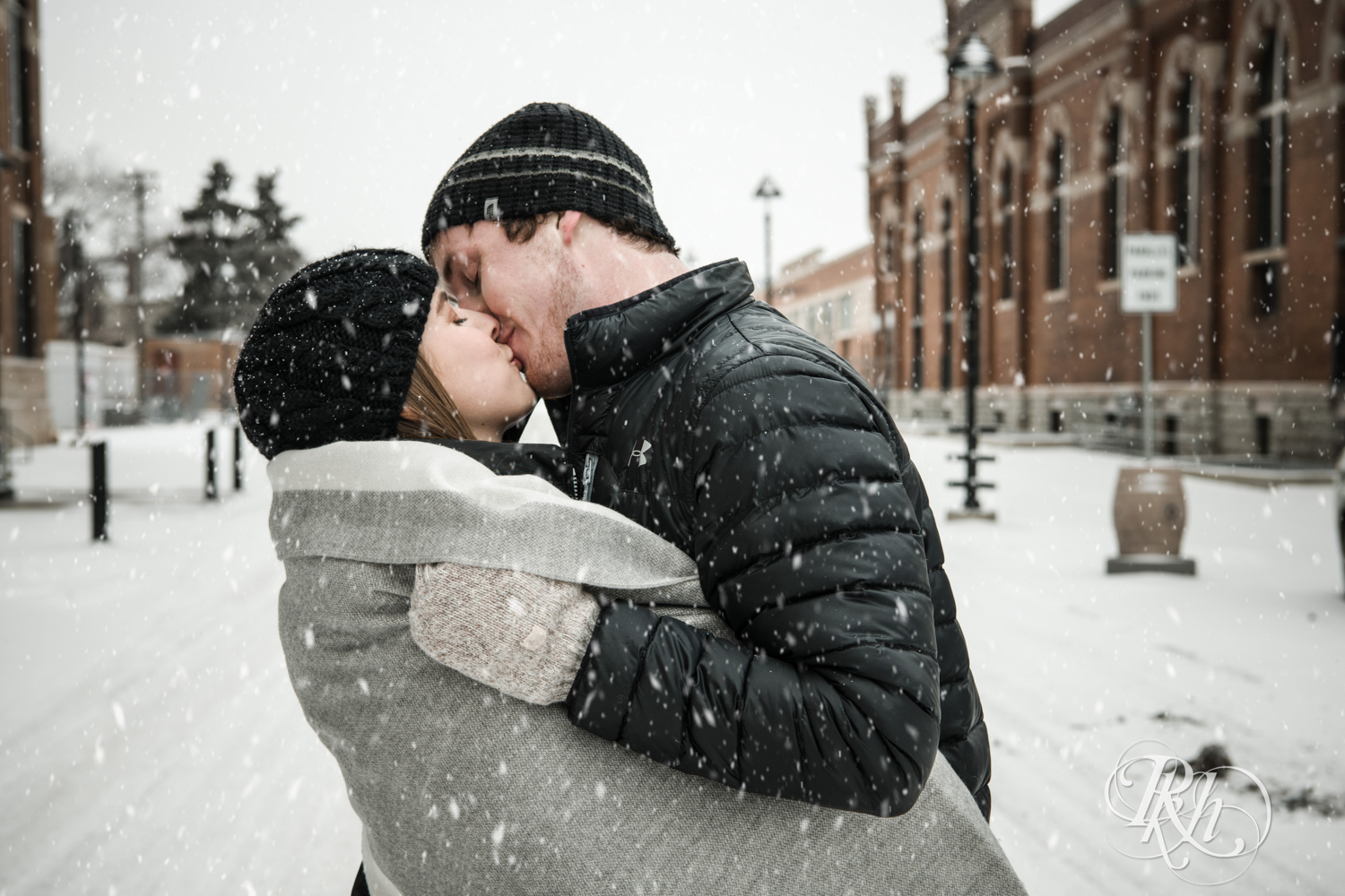 Man and woman kiss in the falling snow during winter engagement photos in Saint Paul, Minnesota.