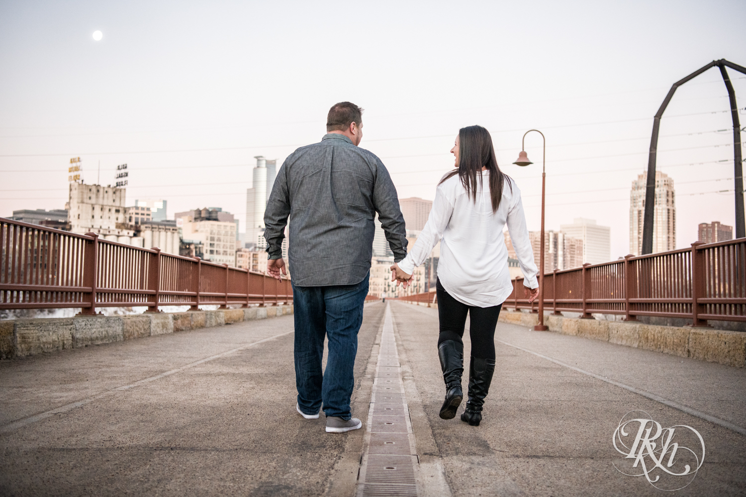 Man and woman walk on the Stone Arch Bridge in Minneapolis, Minnesota at sunrise.