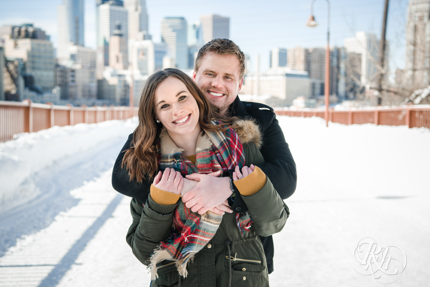 Man and woman hug during winter engagement photography on the Stone Arch Bridge in Minneapolis, Minnesota.