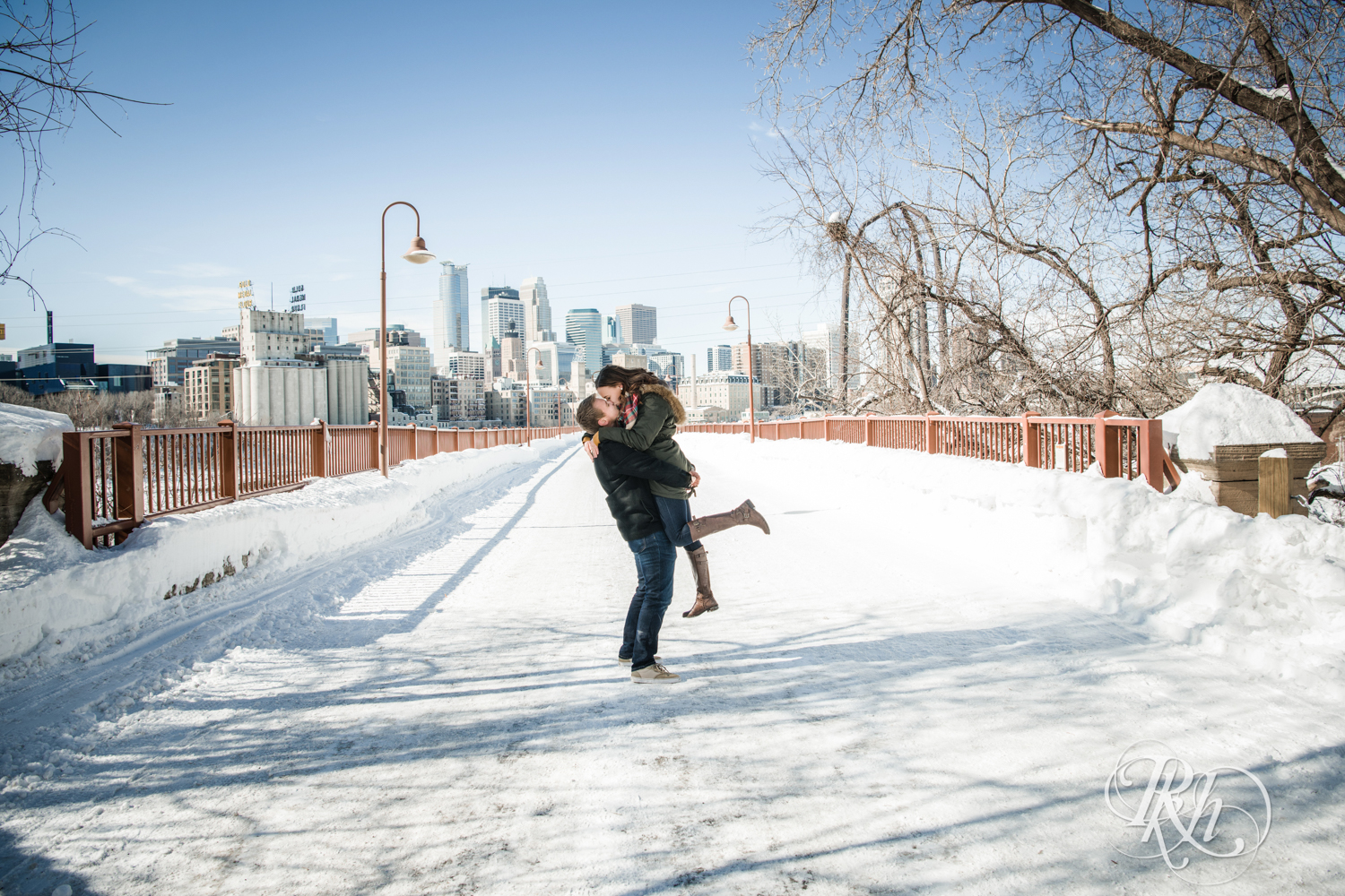 Man and woman kiss during winter engagement photography on the Stone Arch Bridge in Minneapolis, Minnesota.