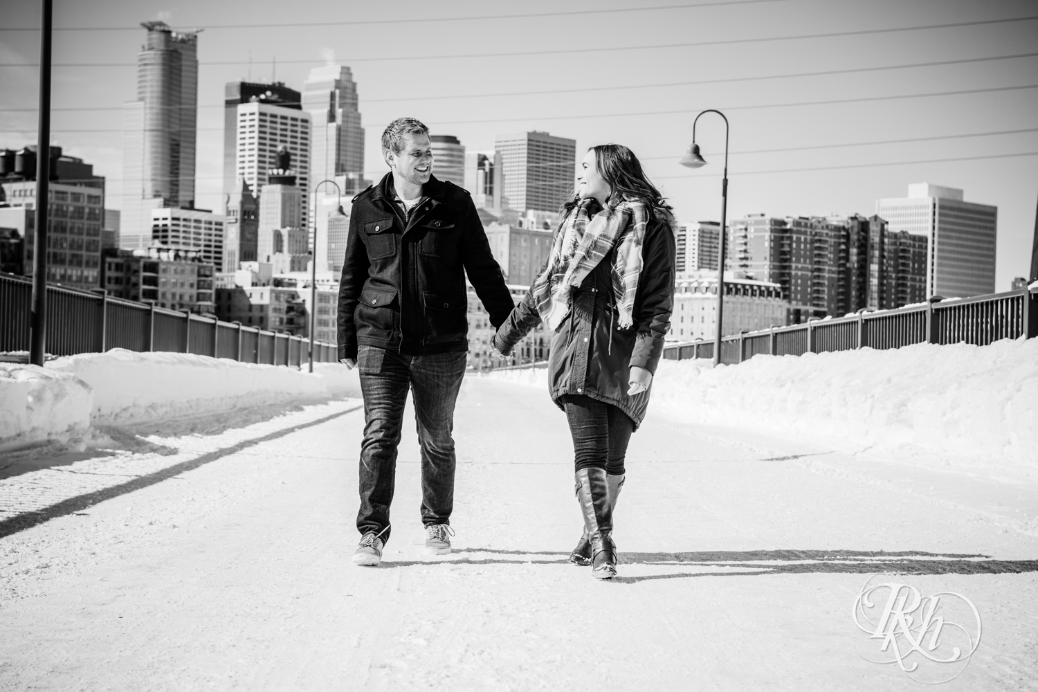 Man and woman smile during winter engagement photography on the Stone Arch Bridge in Minneapolis, Minnesota.