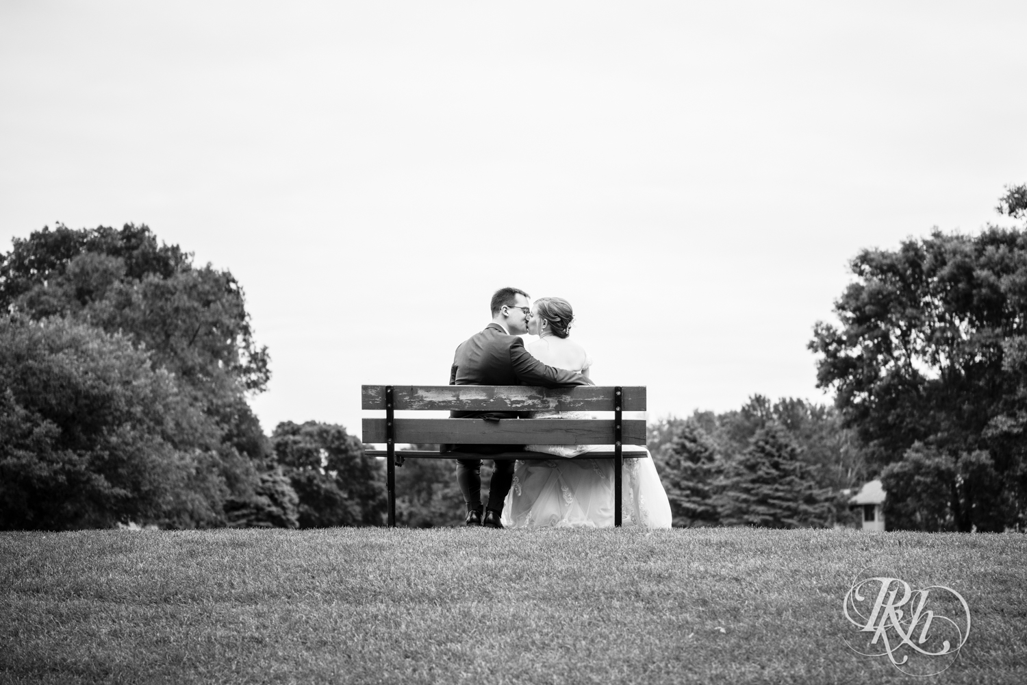 Bride and groom kiss on bench at Oak Glen Golf Course in Stillwater, Minnesota.