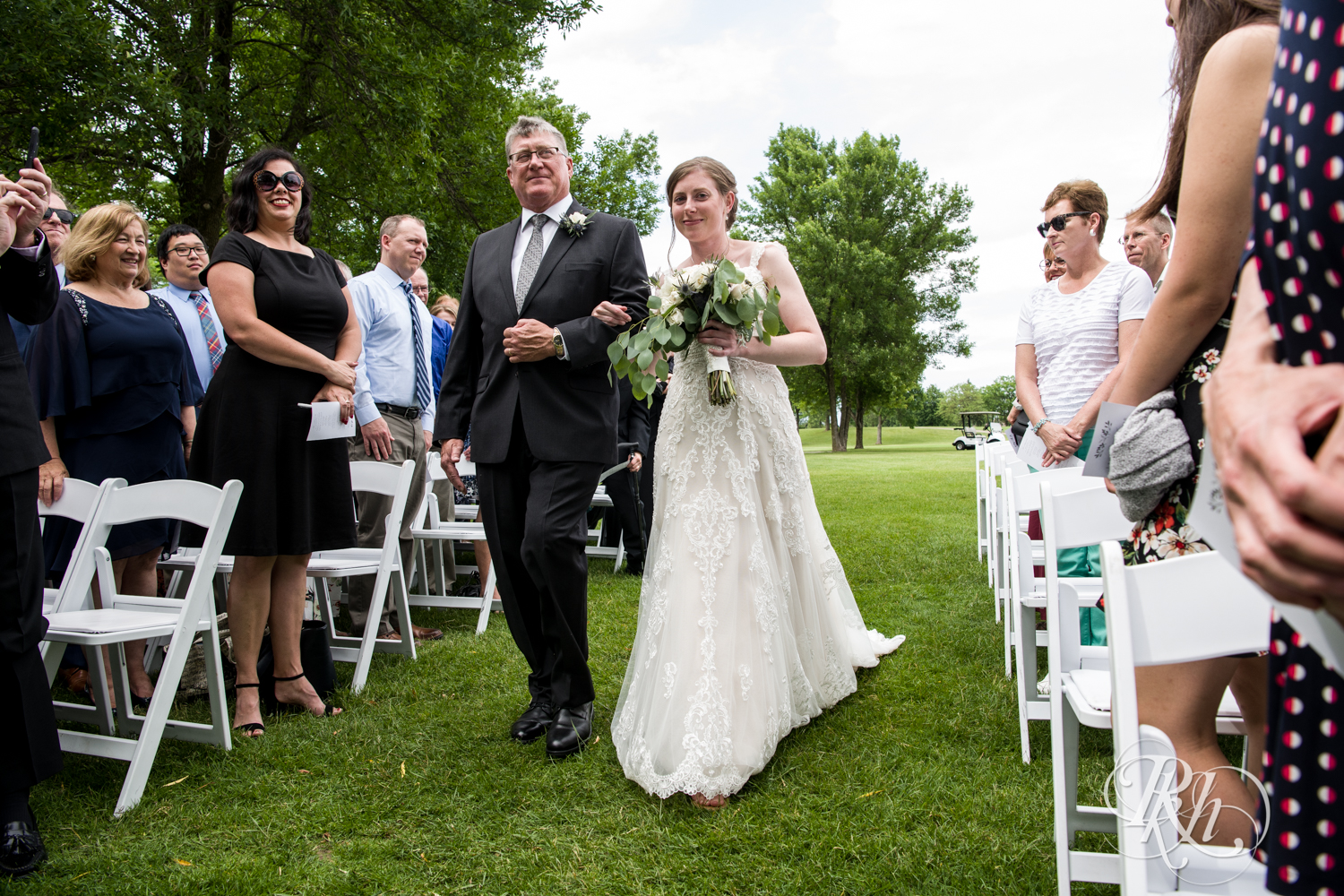 Bride walks down the aisle with dad at ceremony at Oak Glen Golf Course in Stillwater, Minnesota.