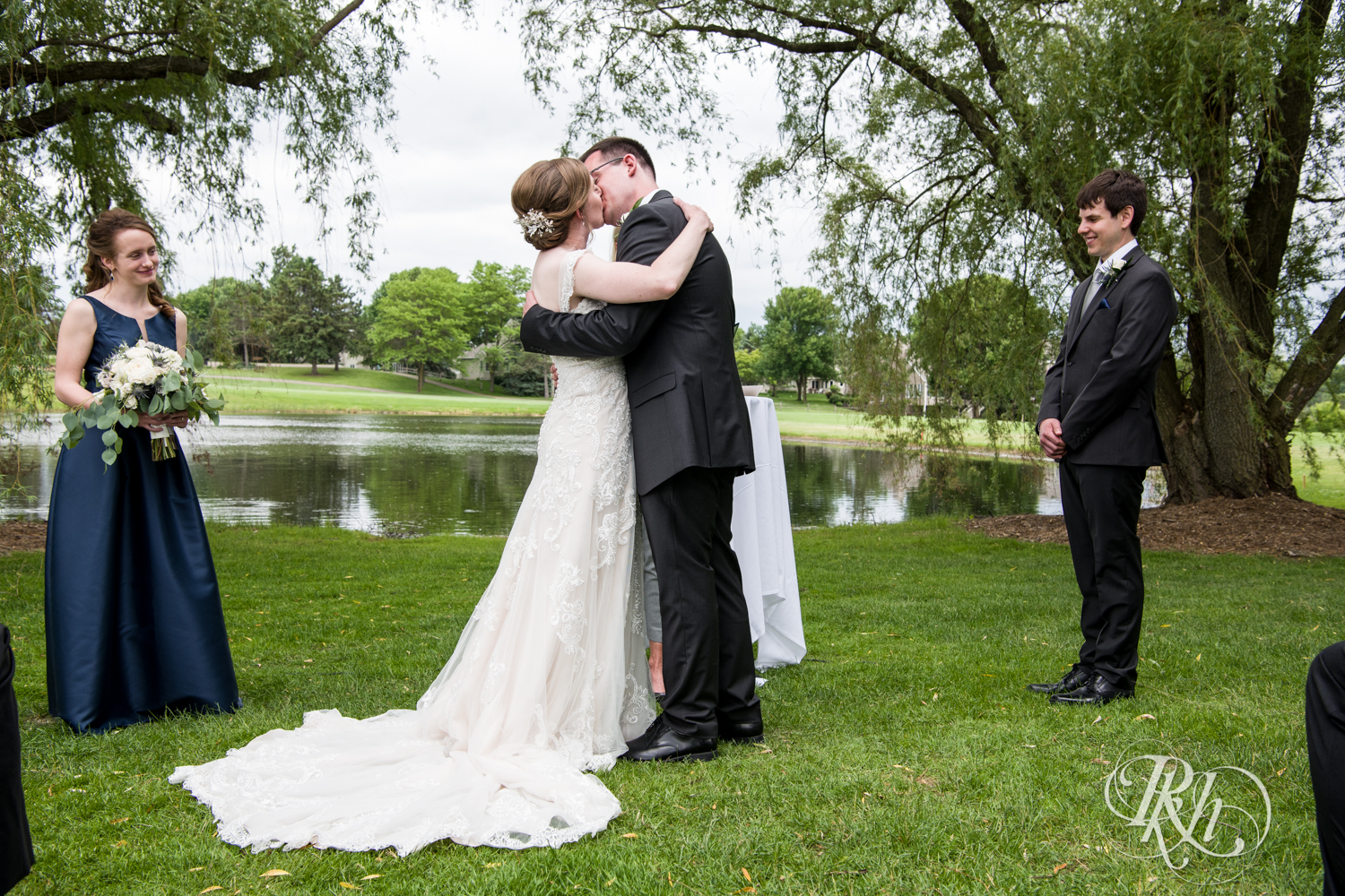 Bride and groom kiss during wedding ceremony at Oak Glen Golf Course in Stillwater, Minnesota.
