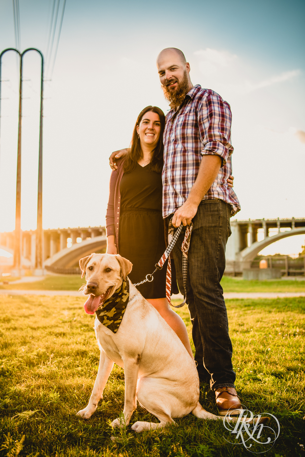 Man and woman smile with Golden Lab puppy in Saint Anthony Main in Minneapolis, Minnesota at sunset.