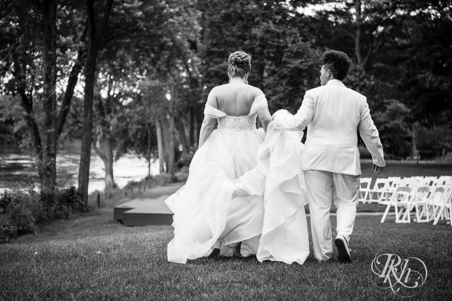 Black lesbian bride and white bride walk together at Leopold's Mississippi Gardens in Brooklyn Park, Minnesota.