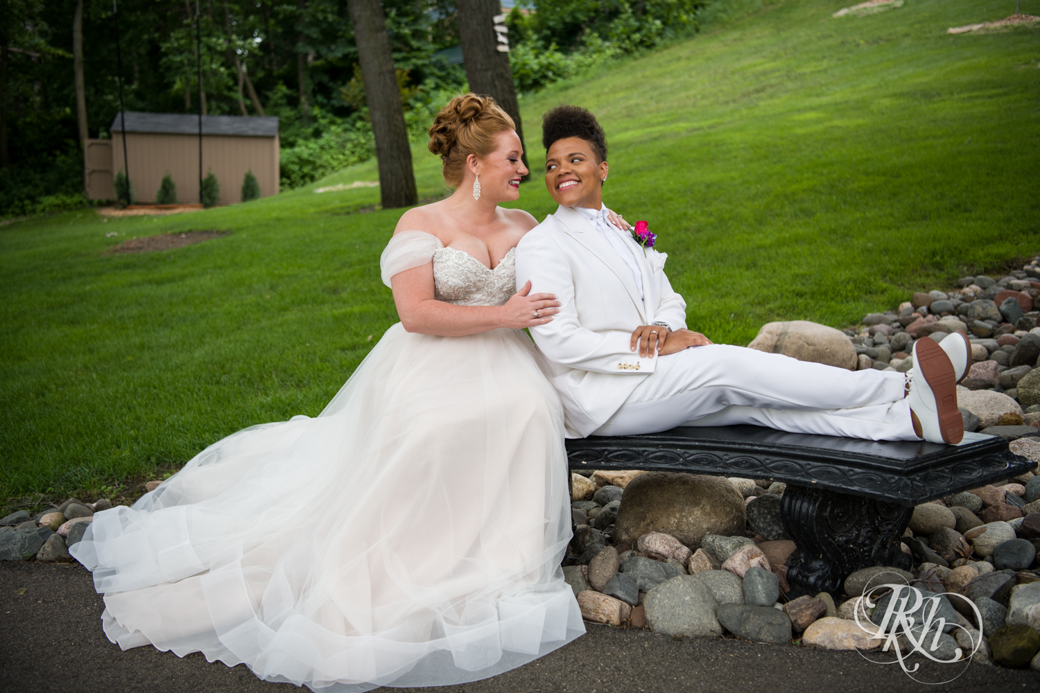 Black lesbian bride and white bride smile at Leopold's Mississippi Gardens in Brooklyn Park, Minnesota.