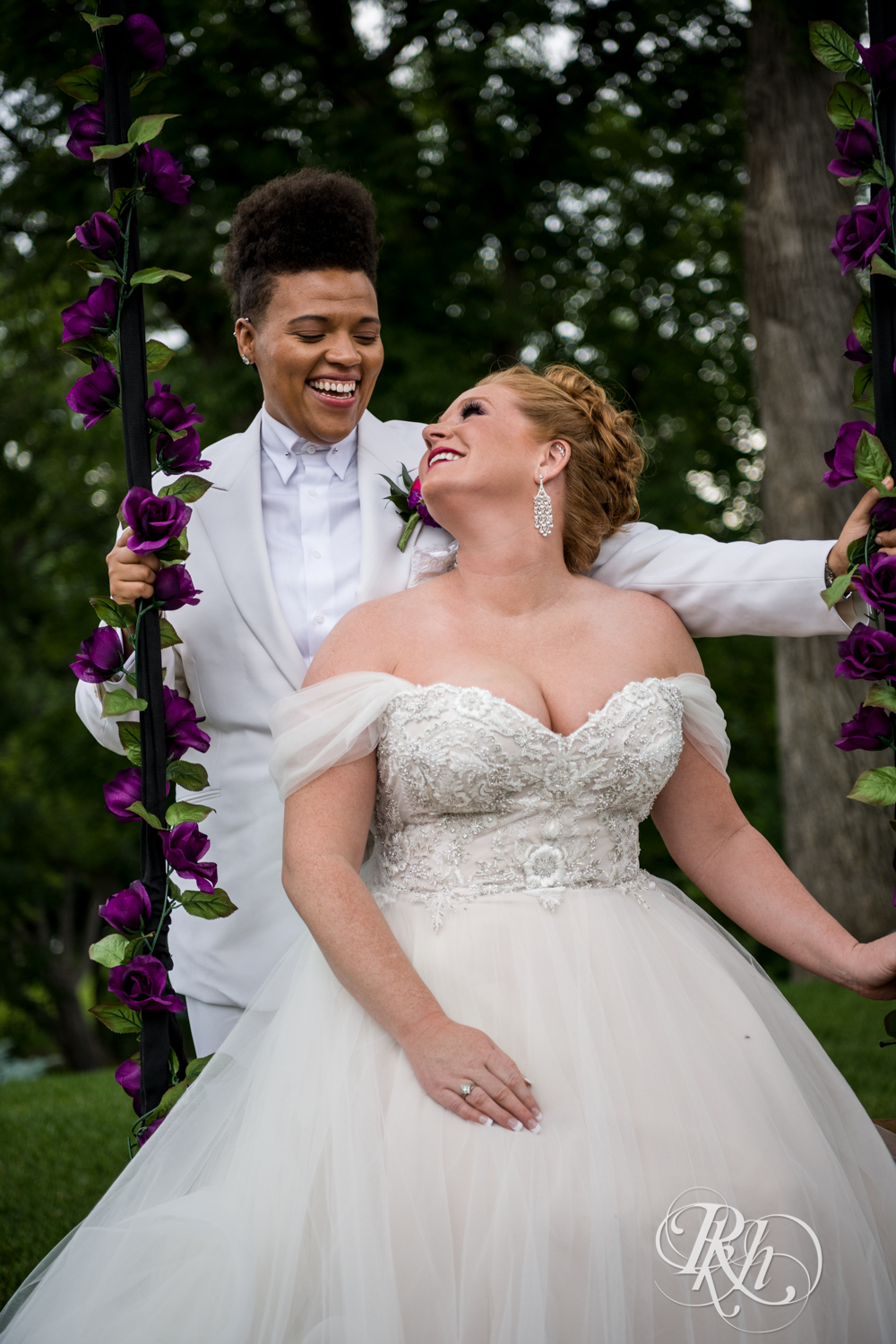 Black lesbian bride and white bride smile at Leopold's Mississippi Gardens in Brooklyn Park, Minnesota.