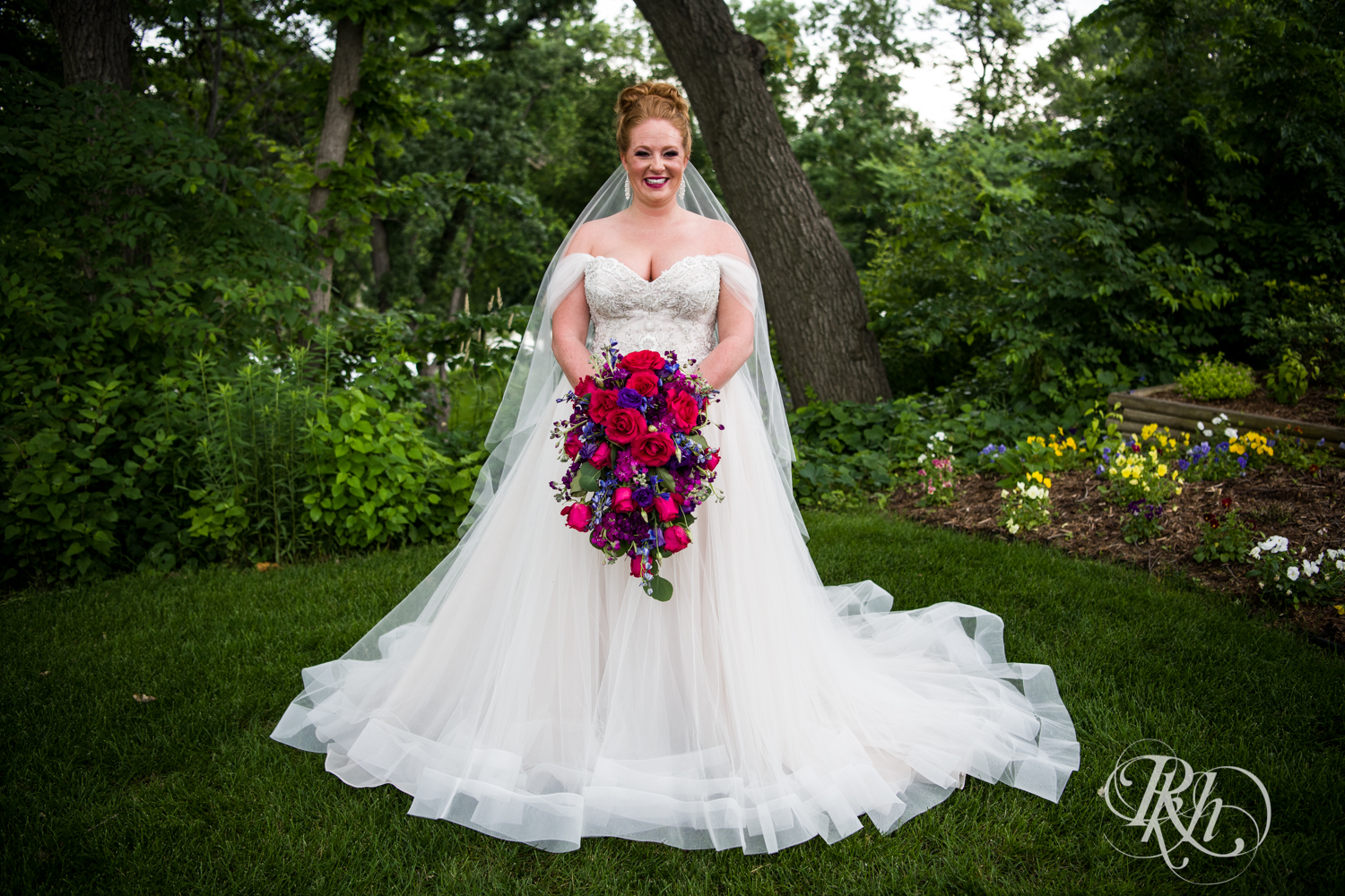 Bride with long veil and colorful flowers smiles at Leopold's Mississippi Gardens in Brooklyn Park, Minnesota.