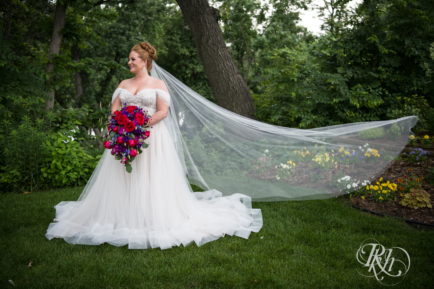 Bride with long veil and colorful flowers smiles at Leopold's Mississippi Gardens in Brooklyn Park, Minnesota.