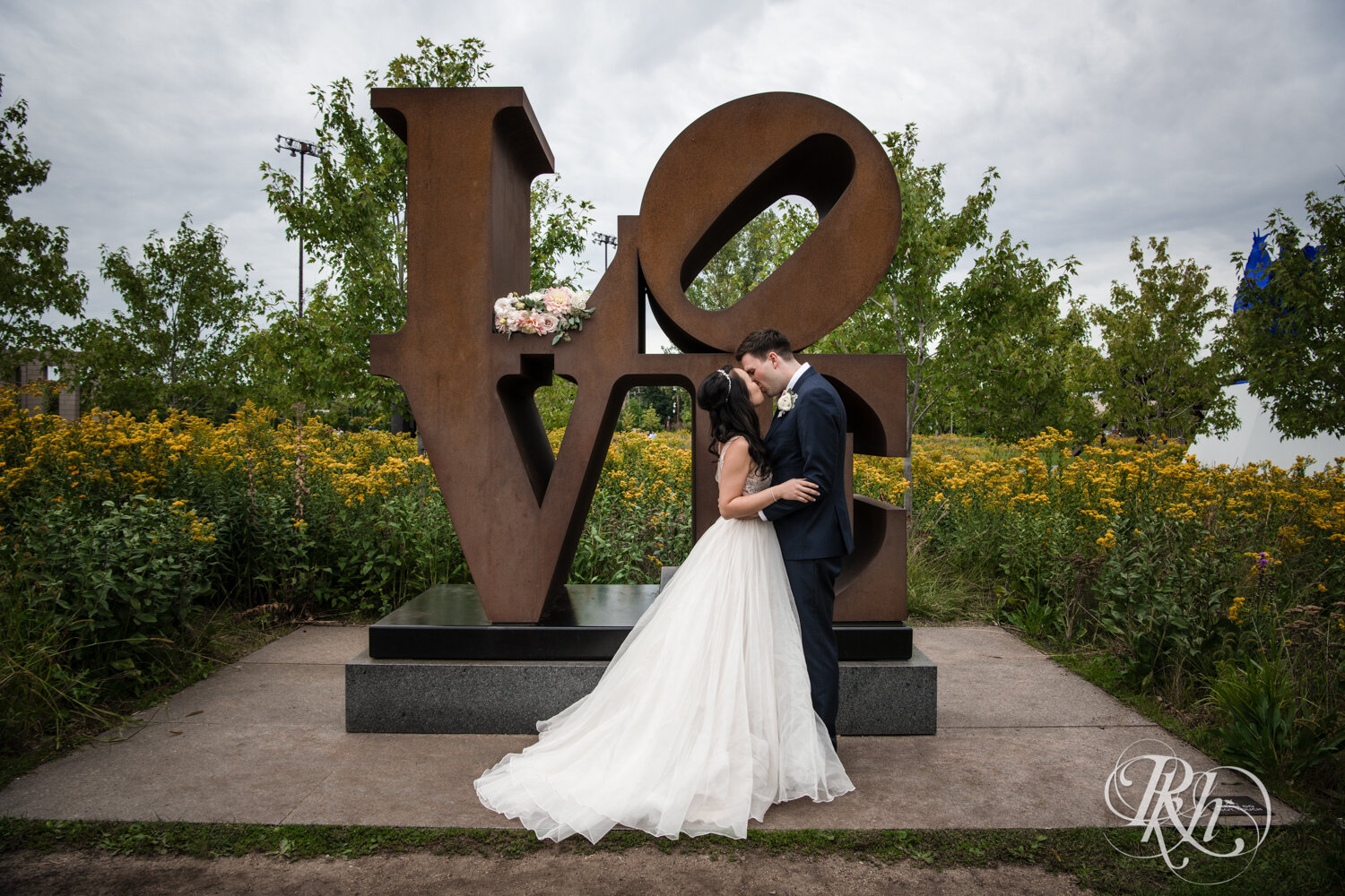 Asian bride and groom kiss in front of LOVE sign in Sculpture Garden in Minneapolis, Minnesota.