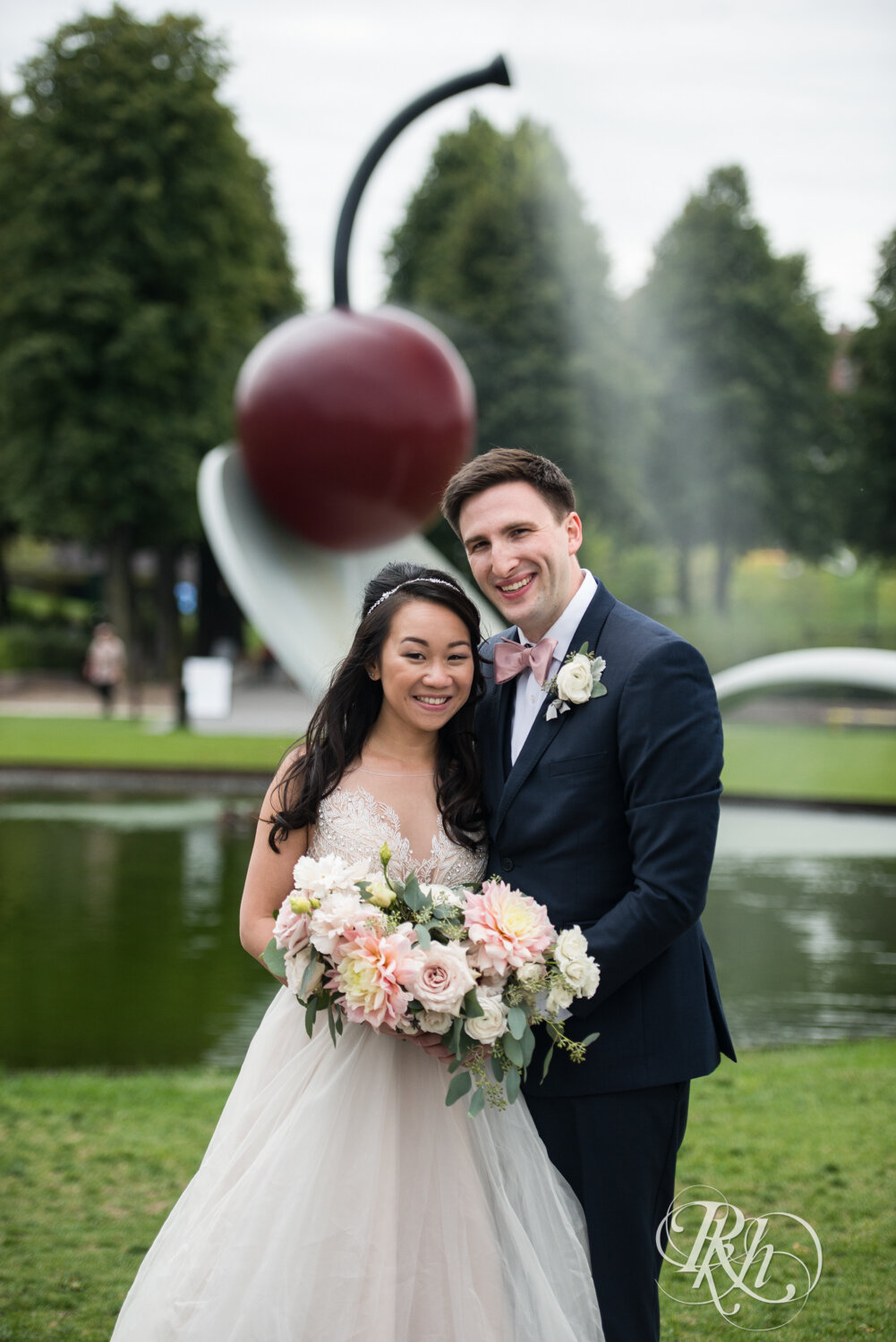 Asian bride and groom kiss in front Spoonbridge and Cherry in Sculpture Garden in Minneapolis, Minnesota.