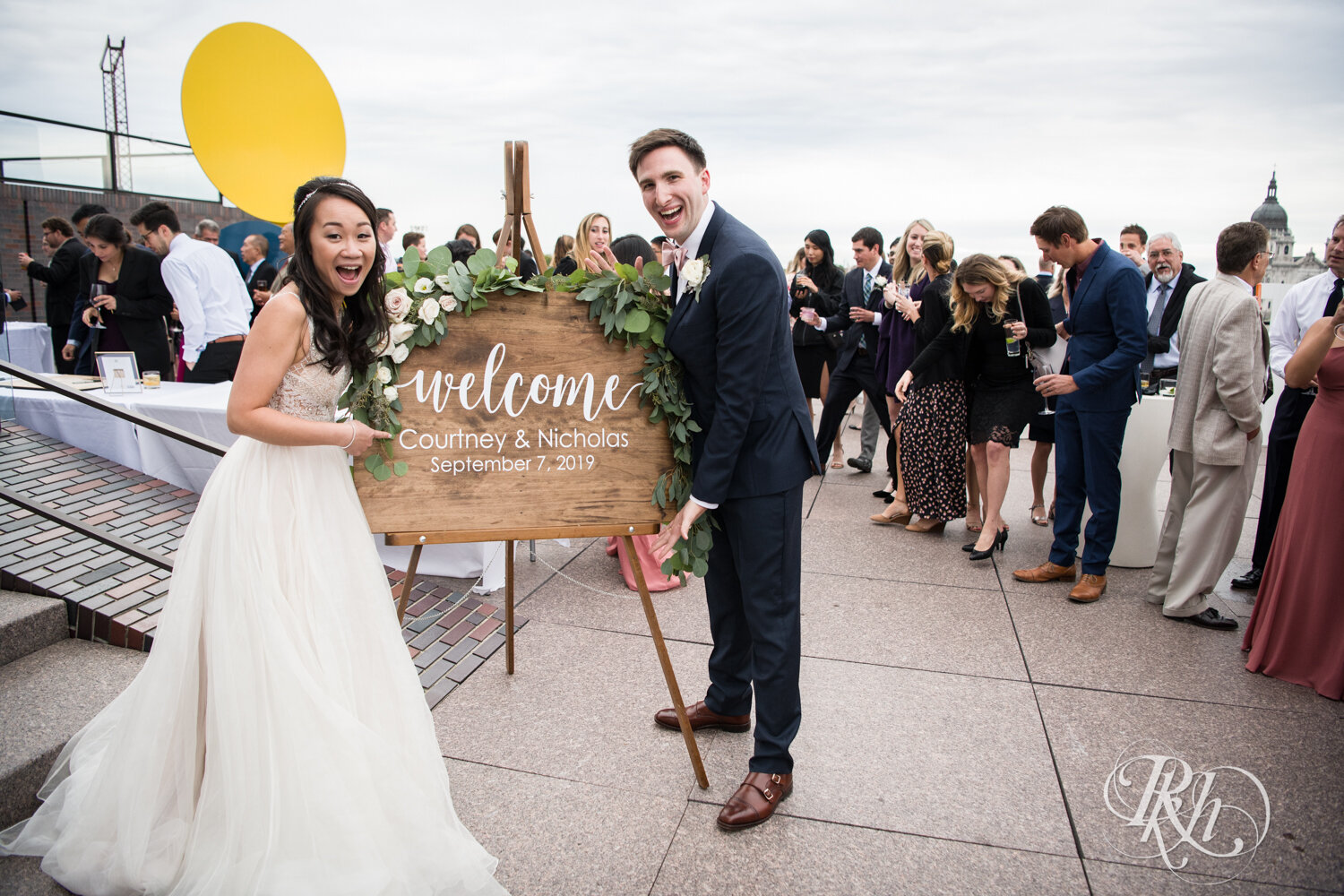 Bride and groom pose by welcome sign on rooftop of Walker Art Center in Minneapolis, Minnesota. 