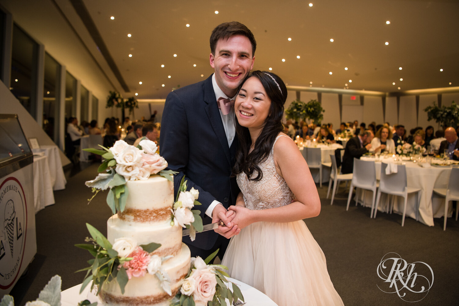 Asian bride and groom cut cake during wedding reception at Walker Art Center in Minneapolis, Minnesota. 