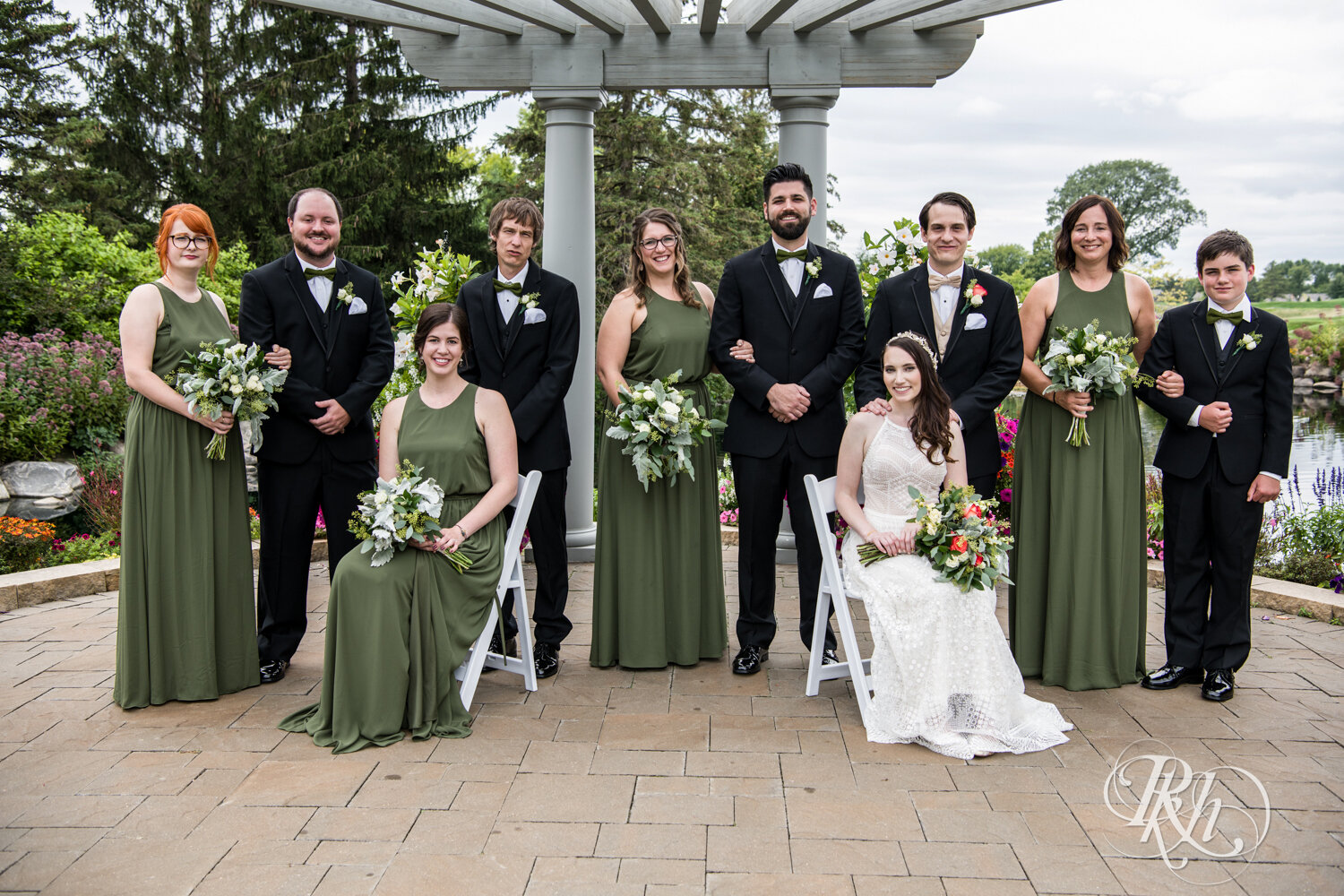 Wedding party in green dresses and black suits smile at Olympic Hills Golf Club in Eden Prairie, Minnesota.
