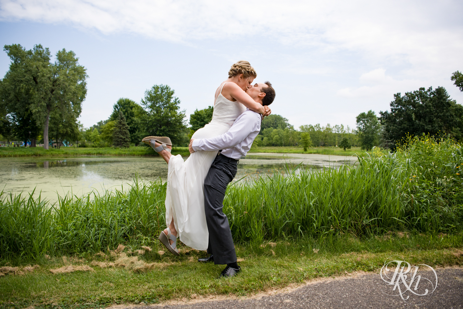 Bride and groom kiss in front of pond at Brookview Golf Course in Golden Valley, Minnesota.