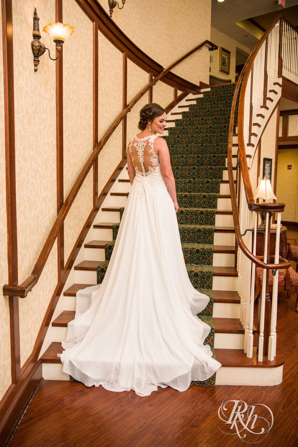 Bride smiles looking over shoulder on stairs at Crown Room in Rogers, Minnesota.