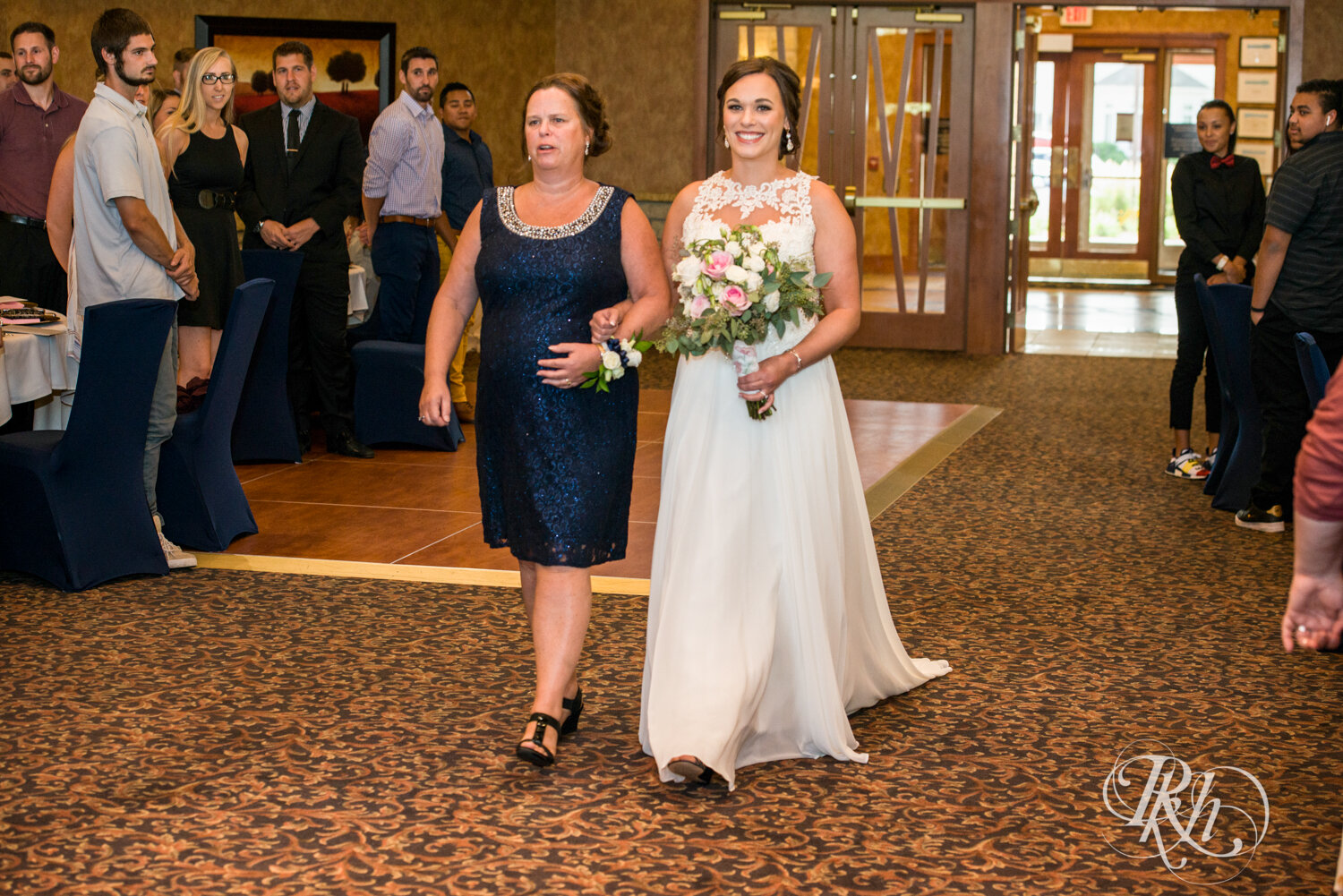 Bride walks down the aisle with mom during indoor wedding ceremony at Crown Room in Rogers, Minnesota.