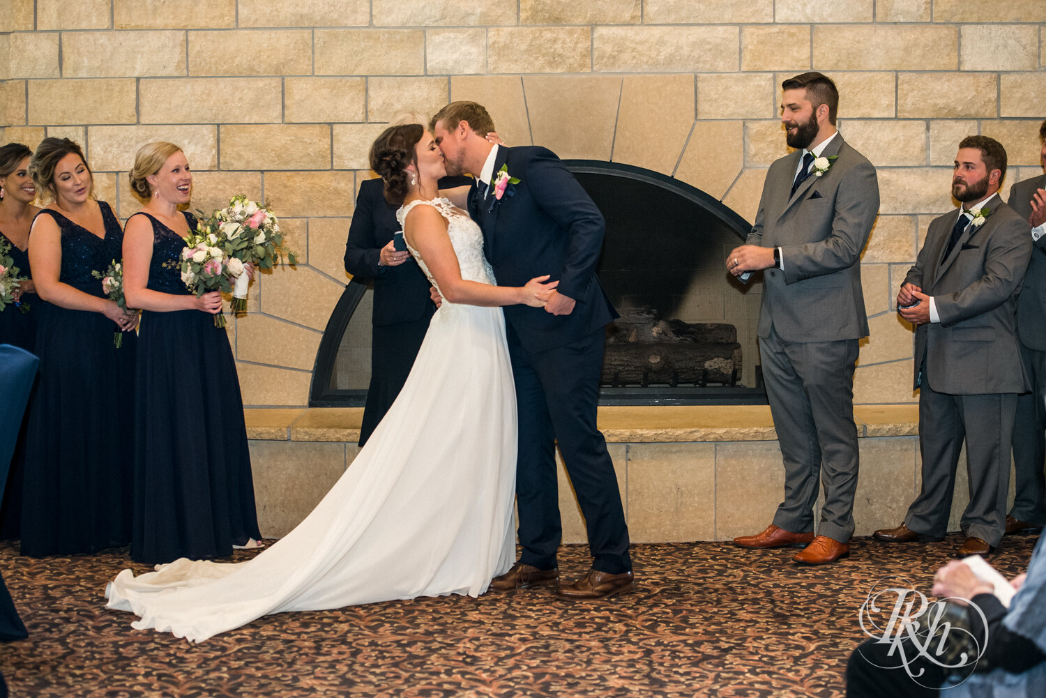 Bride and groom kiss during indoor wedding ceremony at Crown Room in Rogers, Minnesota.