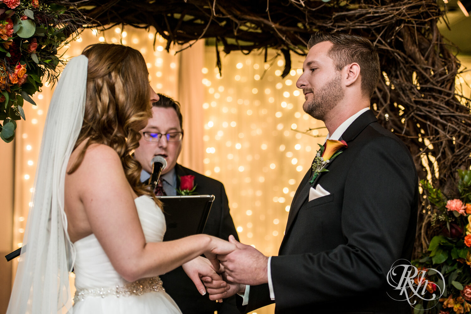 Bride and groom hold hands at indoor wedding ceremony at Rockwoods in Otsego, Minnesota.