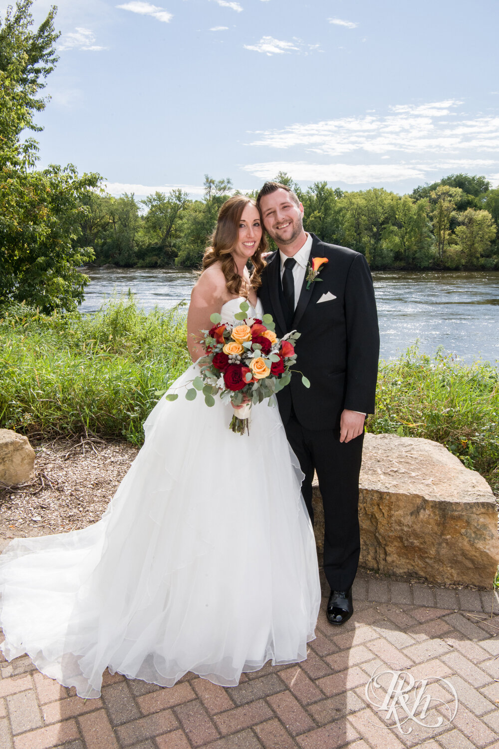 Bride and groom smiling in front of lake in Otsego, Minnesota on sunny wedding day.