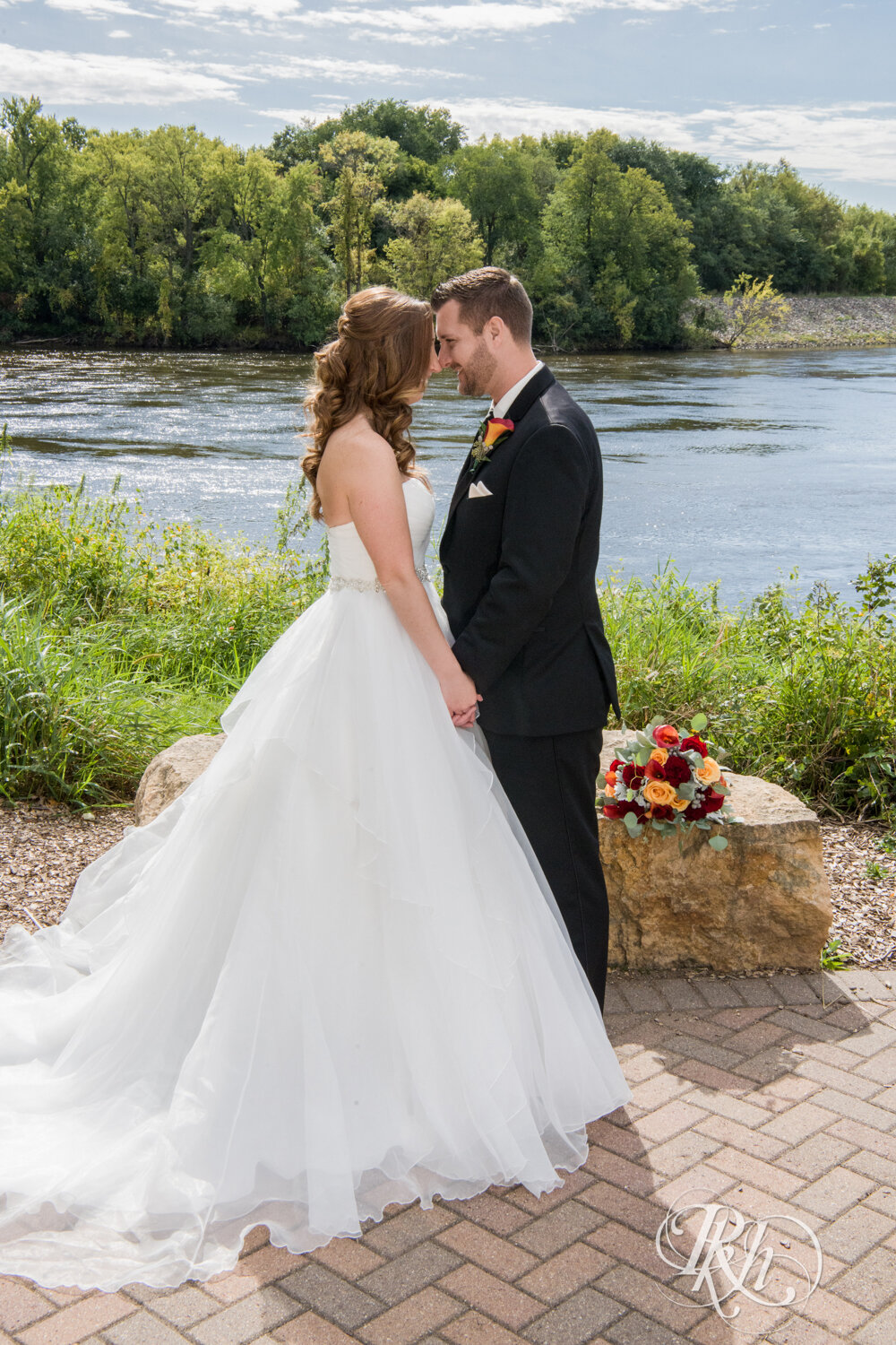 Bride and groom smiling in front of lake in Otsego, Minnesota on sunny wedding day.